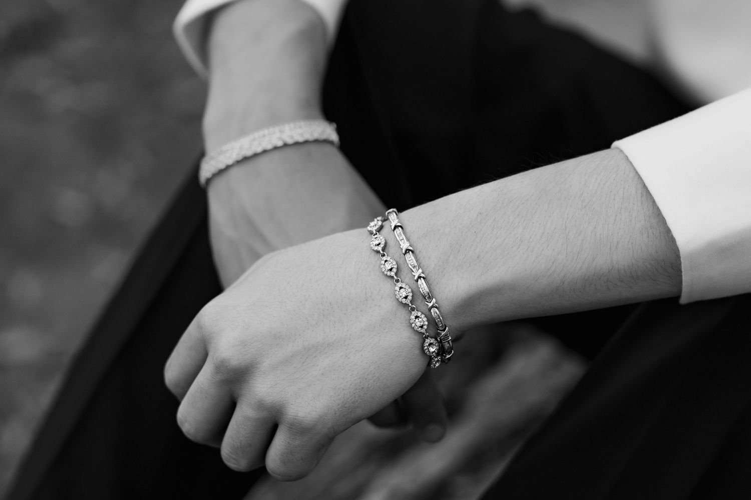 A black and white photo shows a delicate pearl bracelet and ornate silver charm bracelet worn on wrists.