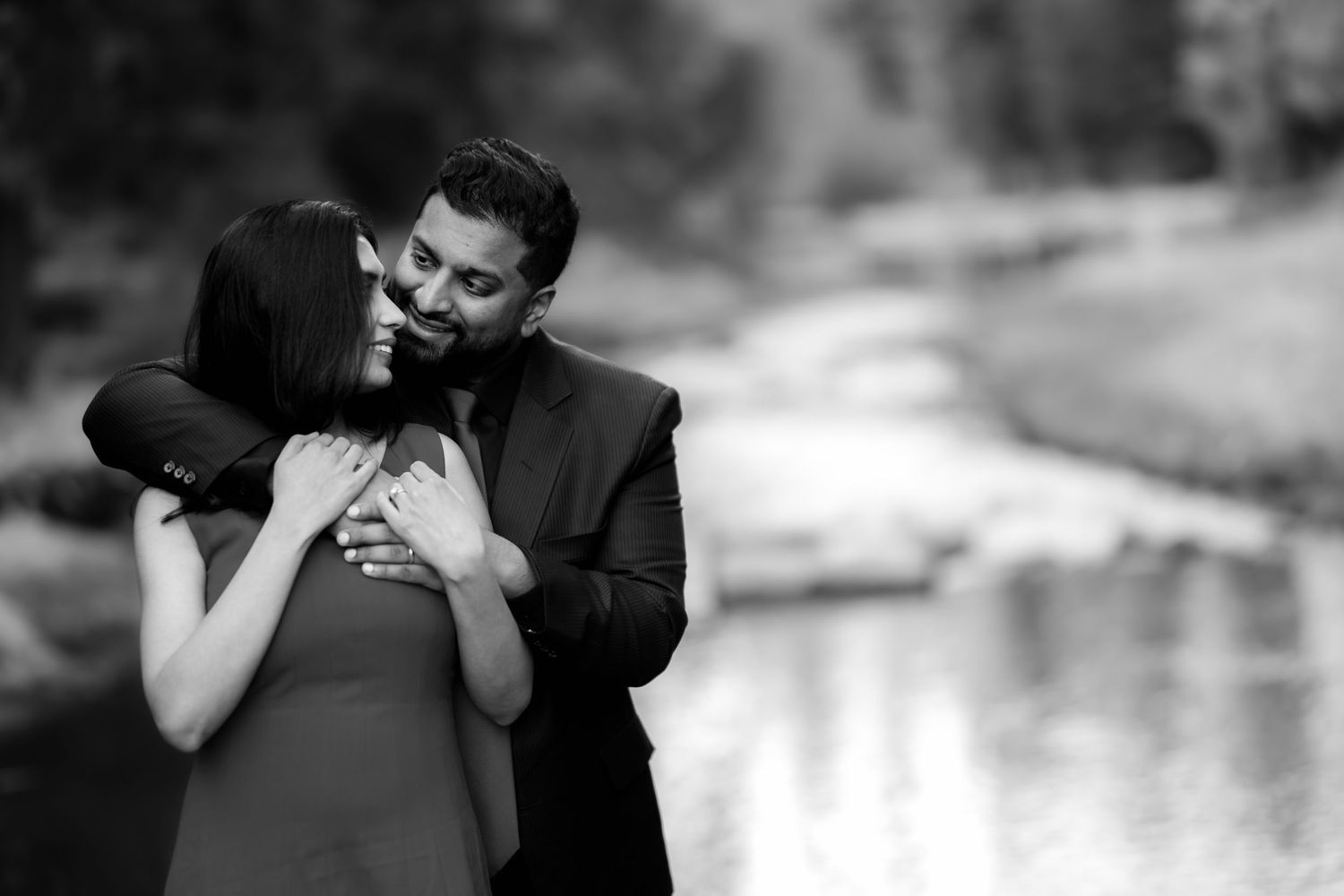 A tender romantic moment captured in black and white as a couple embraces near a reflective pond.