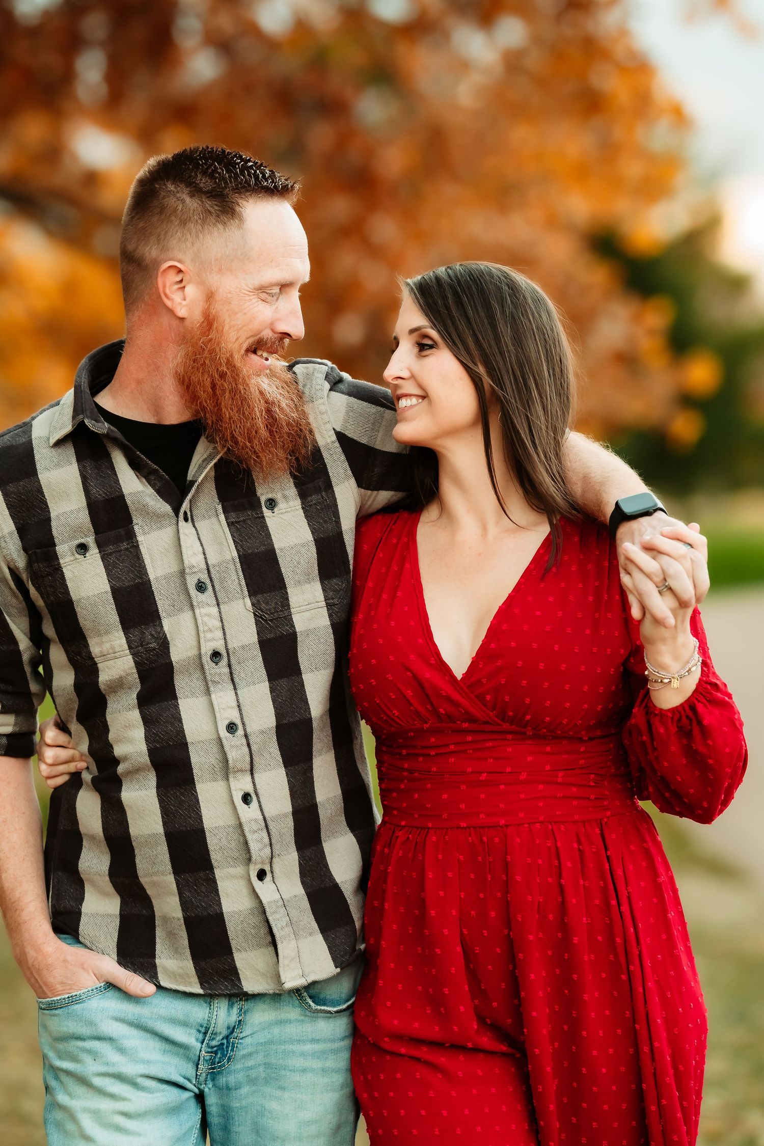 A couple shares intimate moments in coordinating red dress and plaid vest against a warm fall backdrop.