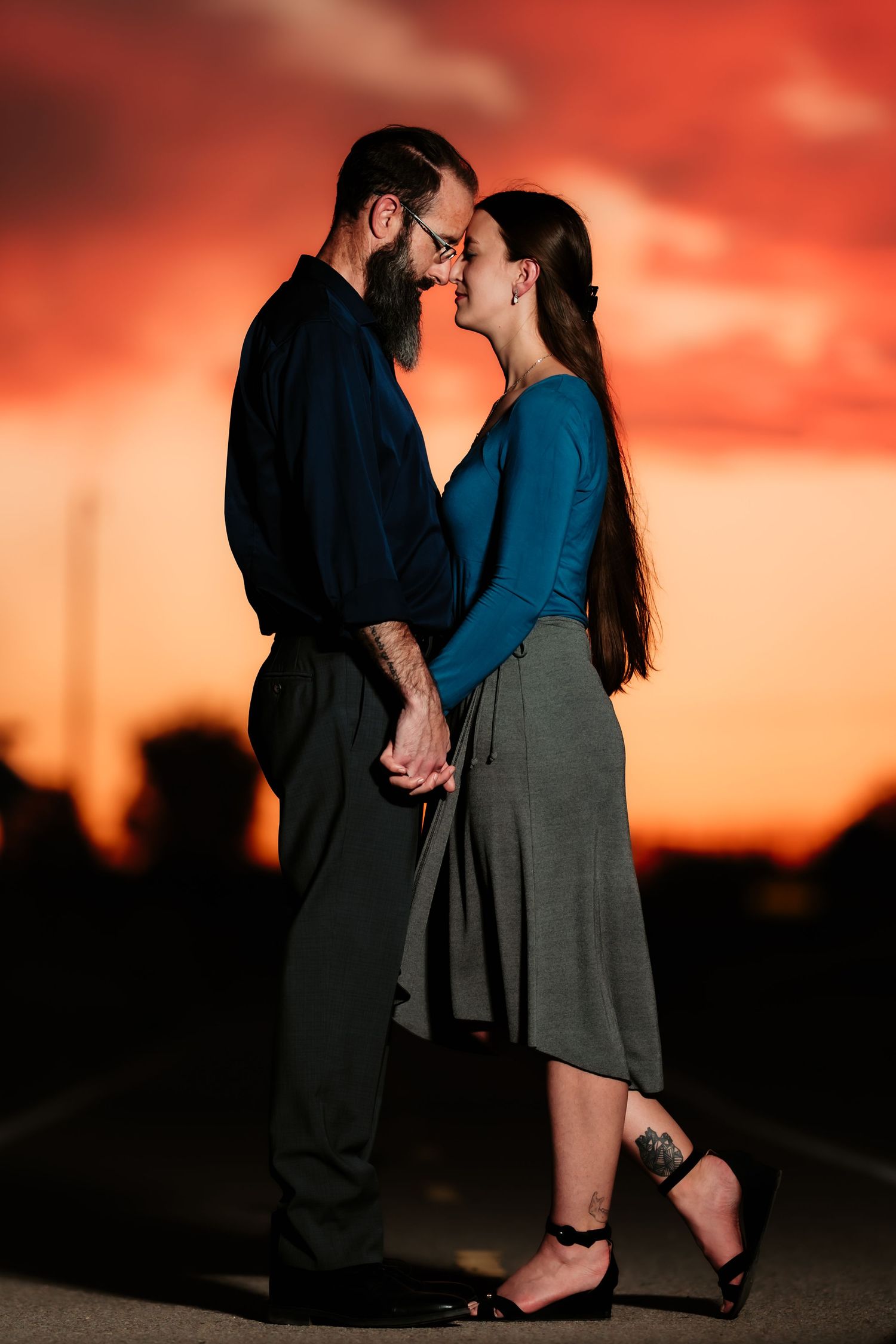 A romantic couple embraces in silhouette against a vibrant red and orange sunset sky.