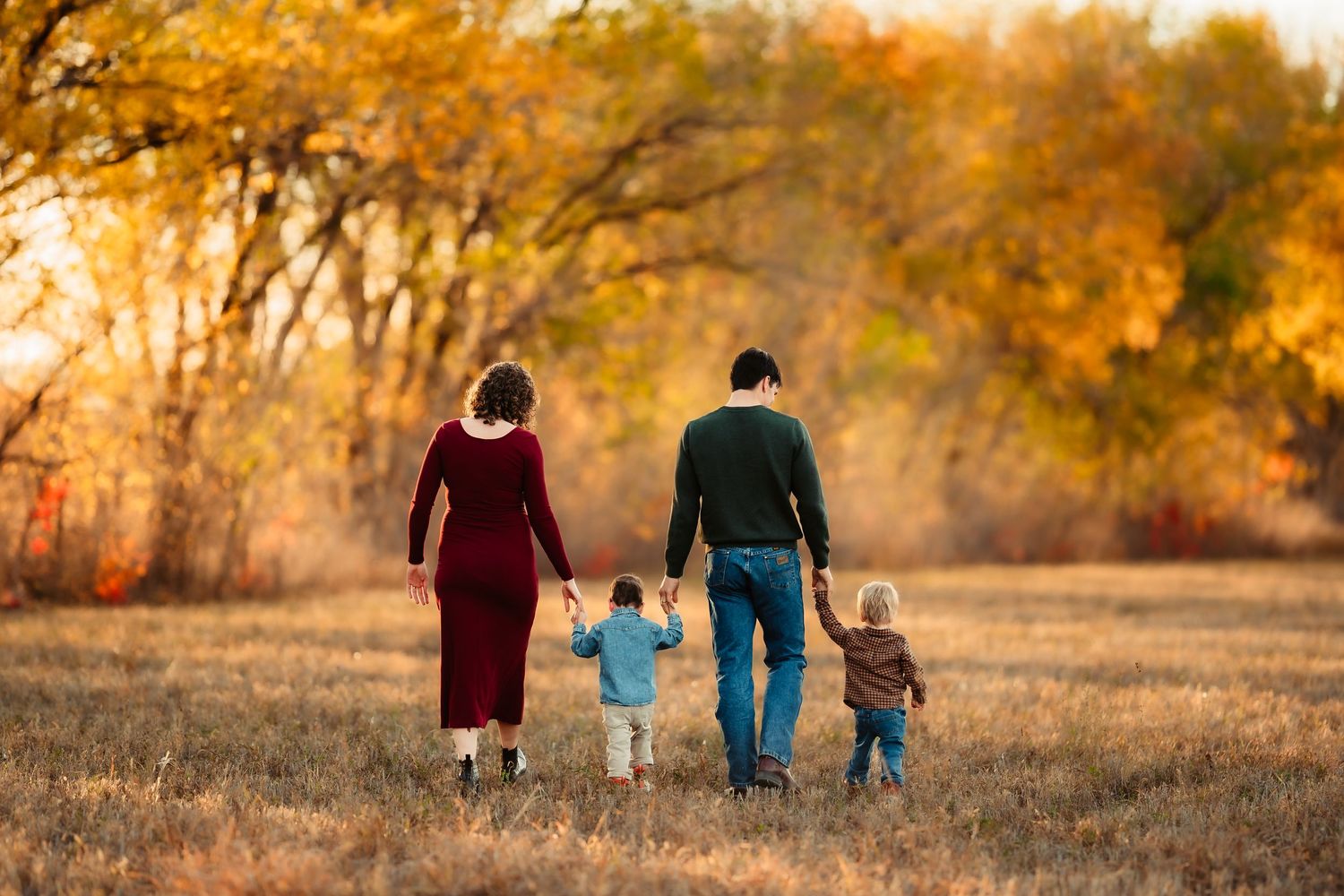 A family walks together through a golden autumn field at sunset holding hands and enjoying the warm fall colors.