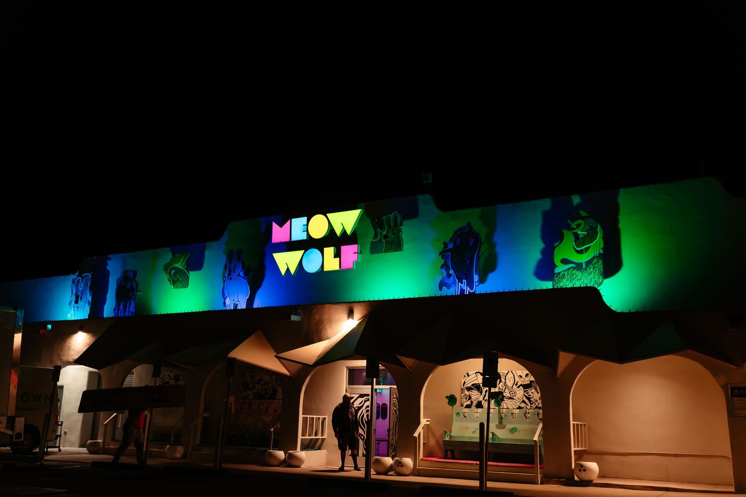 A dark theater stage with dramatic green and blue lighting illuminates performers during a live show.