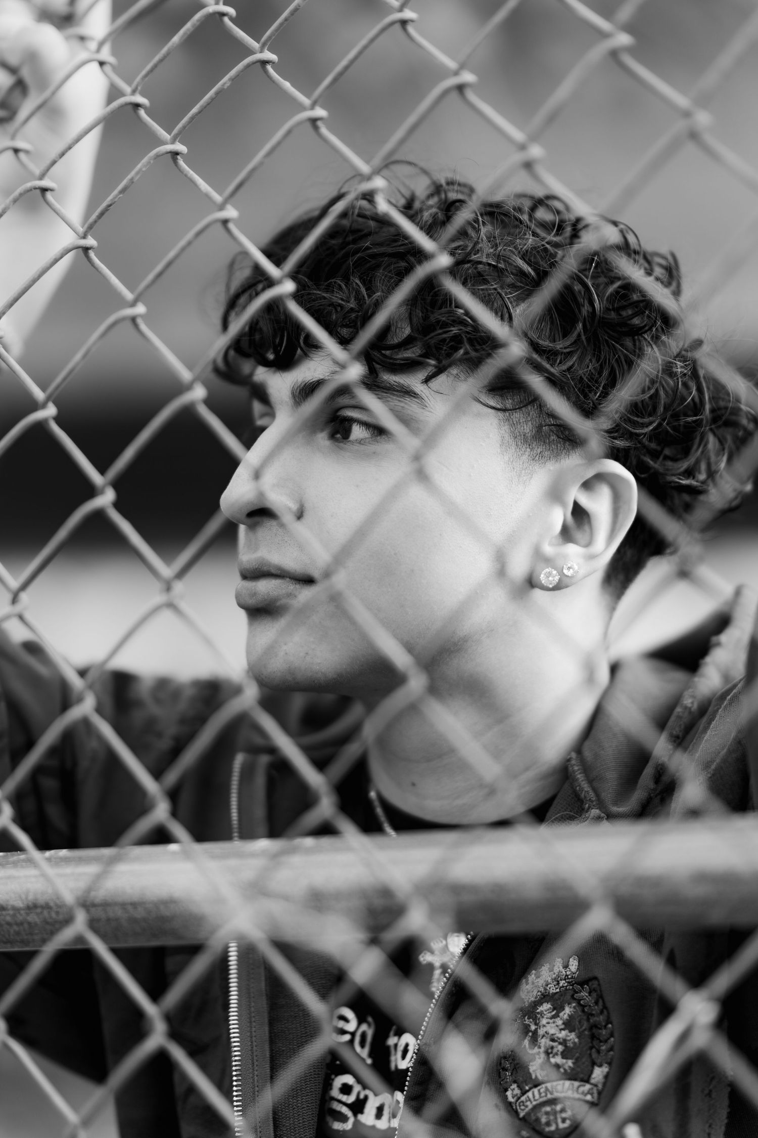 Artistic black and white profile shot through chain link fence showing earring and curly hair.