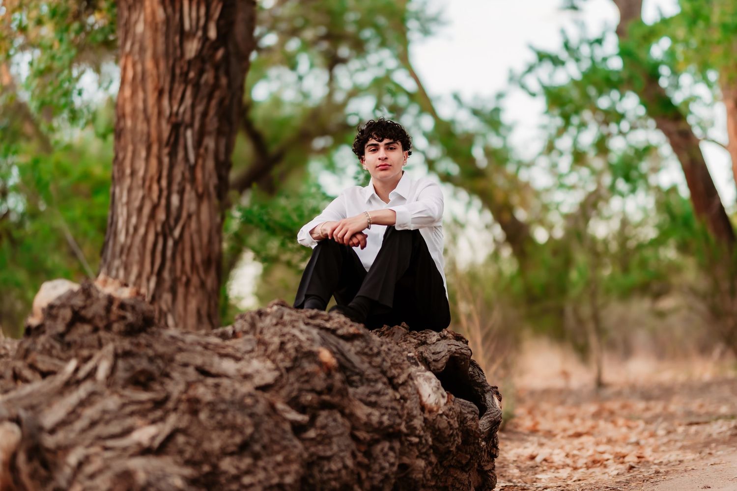 Casual portrait sitting on fallen tree trunk in natural forest setting.