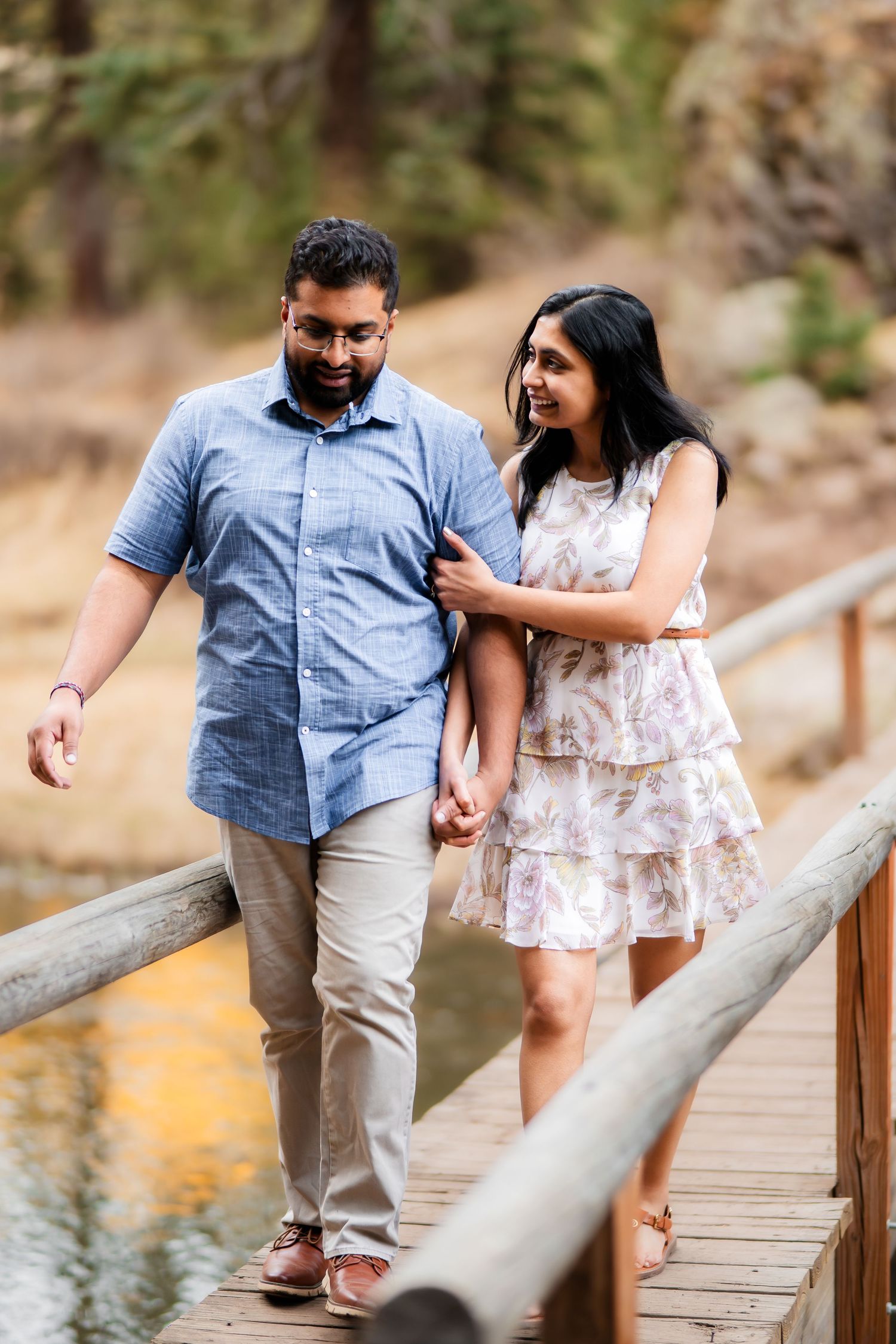 A couple walks hand in hand along a wooden footbridge over a stream.