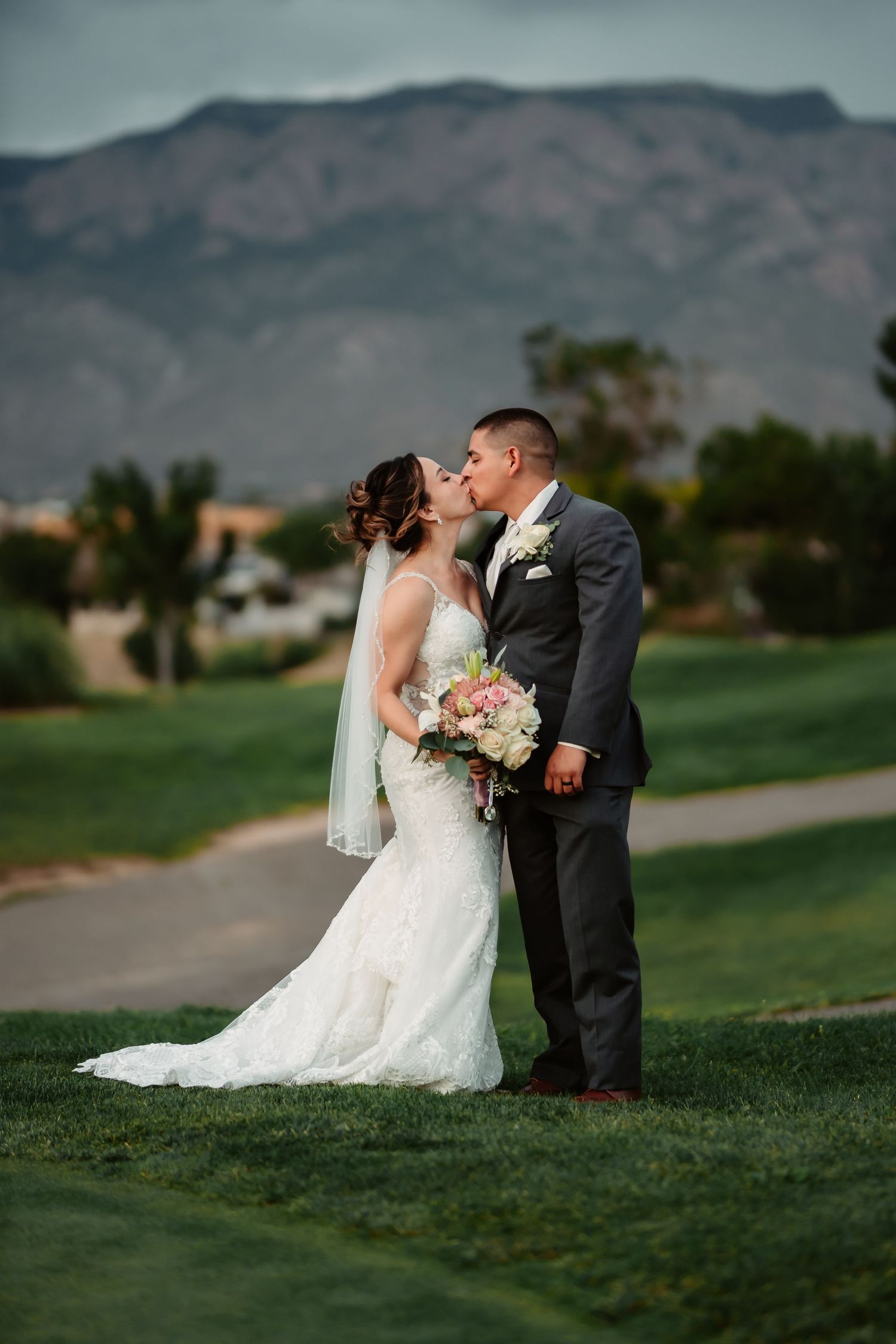 Newlyweds share a romantic moment on a golf course with mountain backdrop.