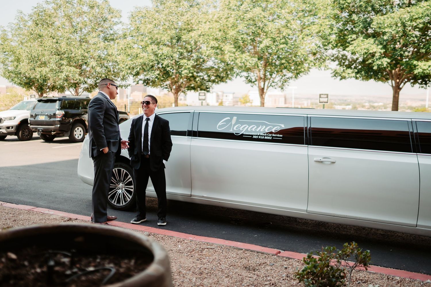 White stretch limousine parked outside with trees and buildings in the background.