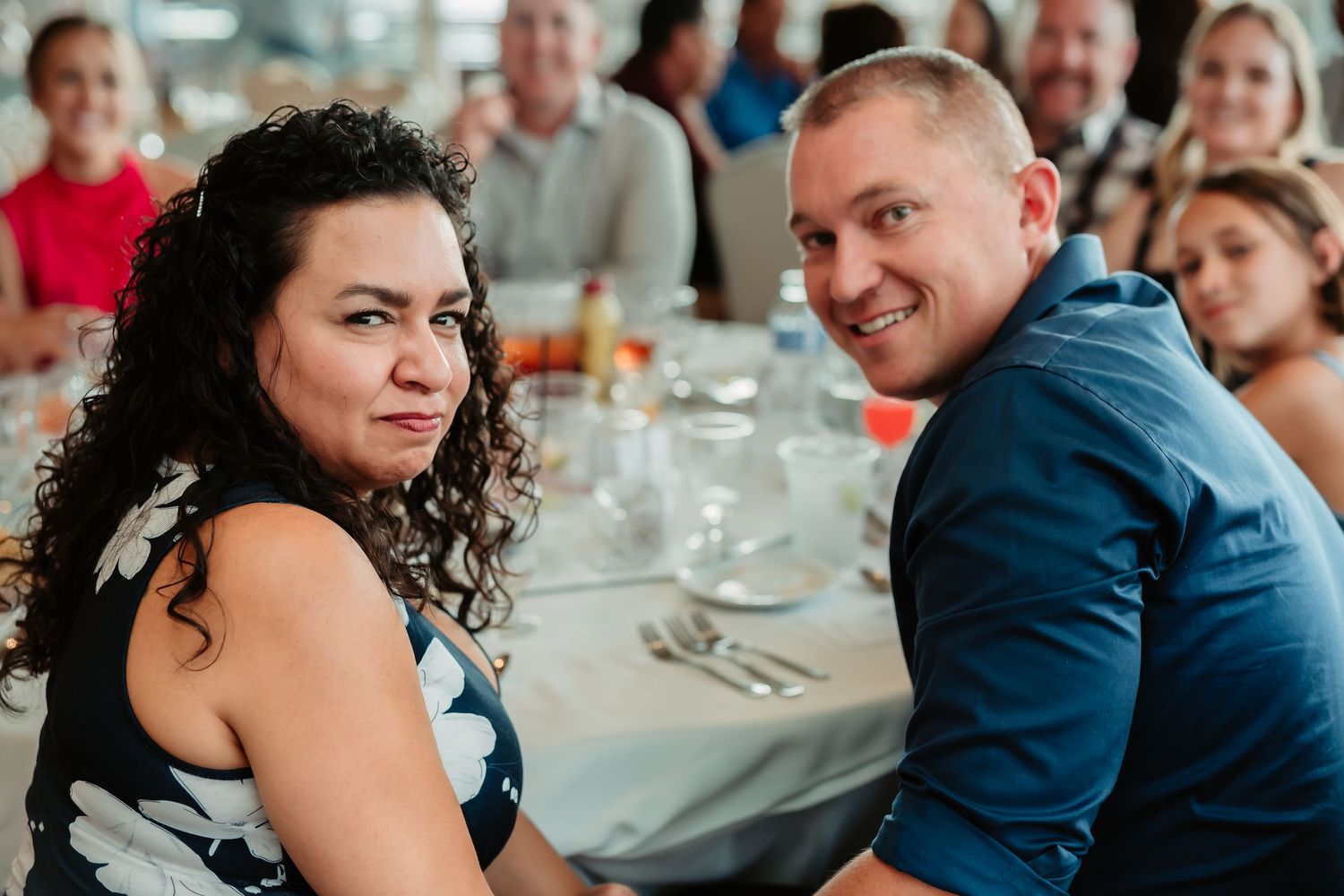 A candid moment captured during a wedding reception with guests seated at decorated tables.