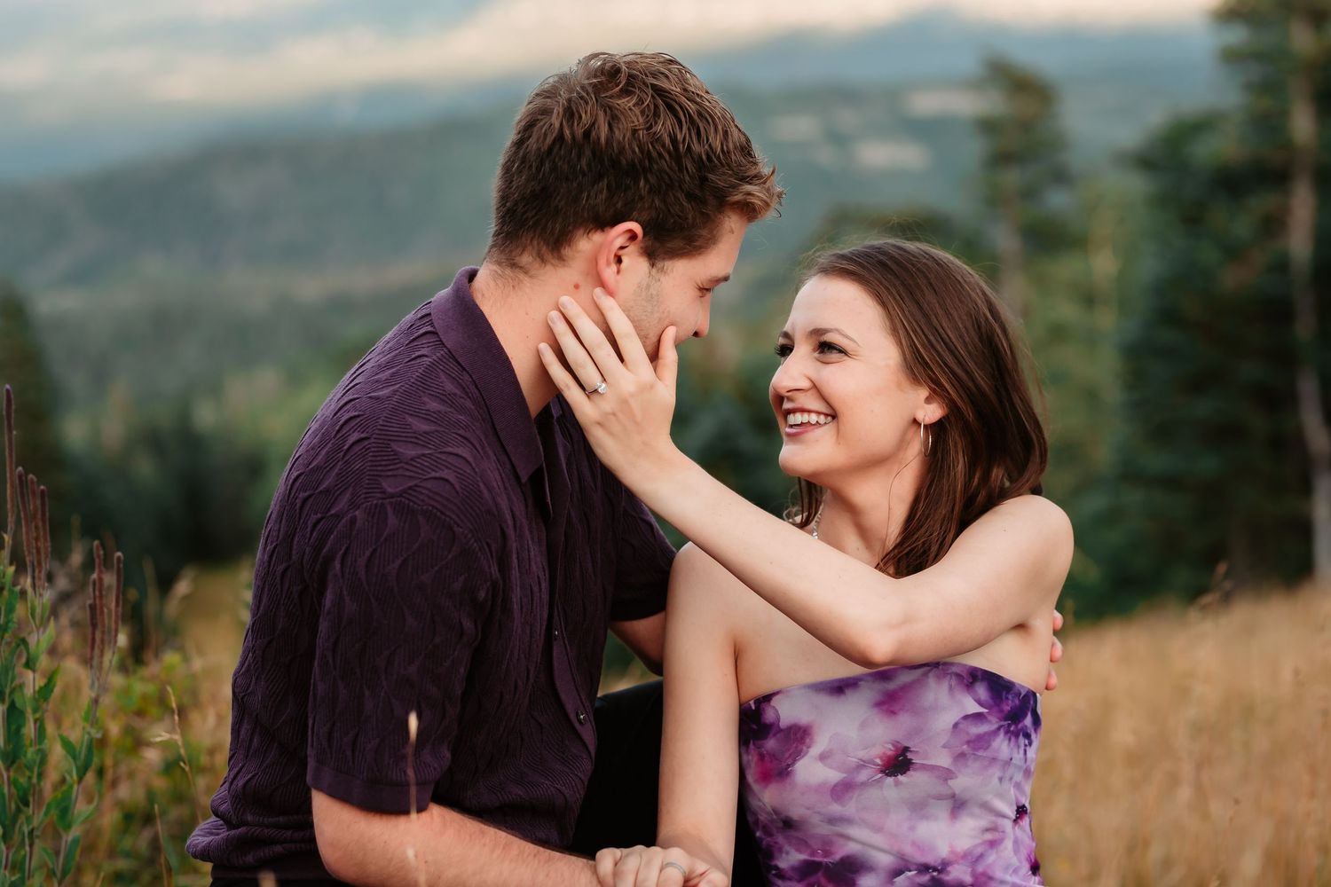Intimate couple poses in a mountain meadow during golden hour with evergreen trees in background.