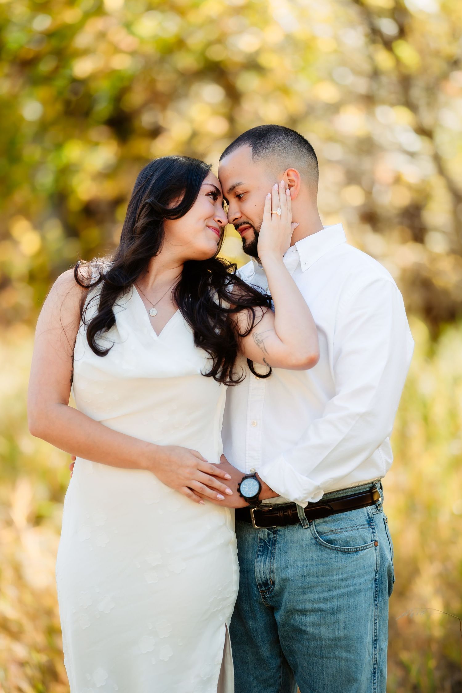 A romantic couple embraces outdoors in golden sunlight during an engagement photo session.