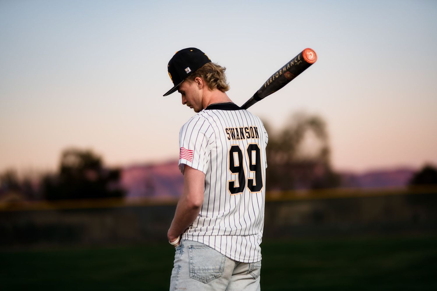 Baseball player wearing jersey number 99 stands with bat at sunset on field.