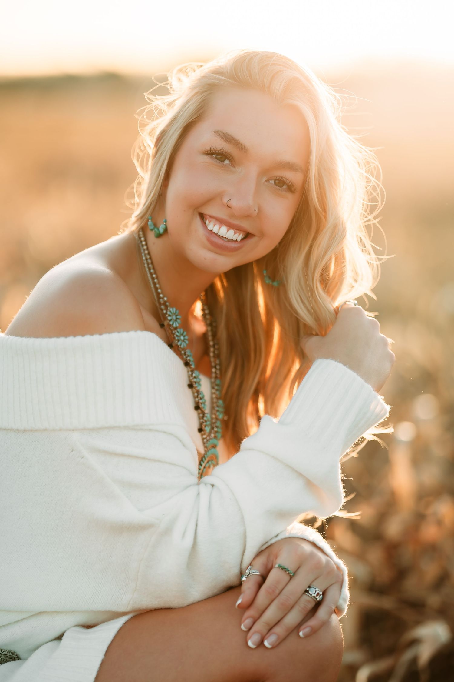 Portrait of someone in a white off-shoulder sweater wearing turquoise jewelry during golden hour sunset.