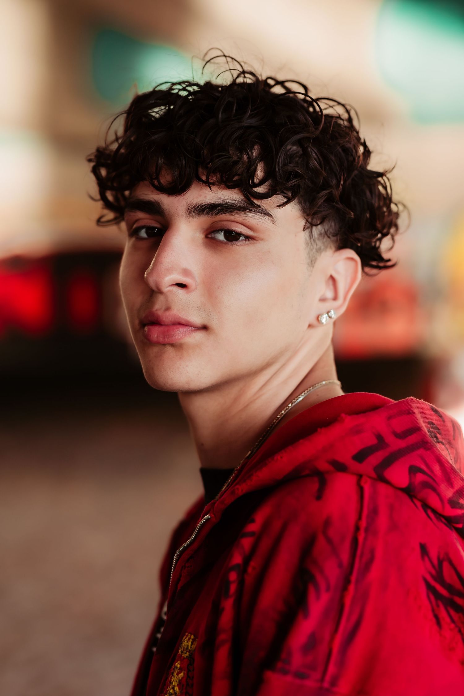Close-up portrait showing curly hair and red hoodie against blurred background.