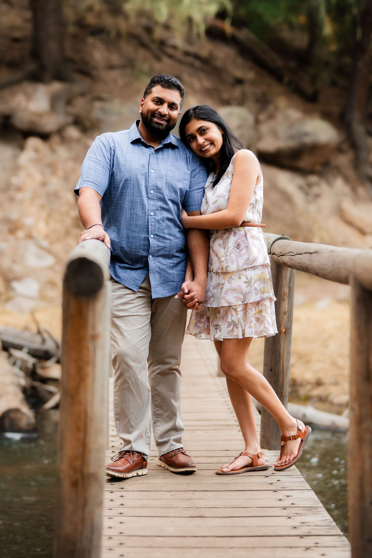 A couple standing close together on a wooden bridge over water in casual outdoor attire.