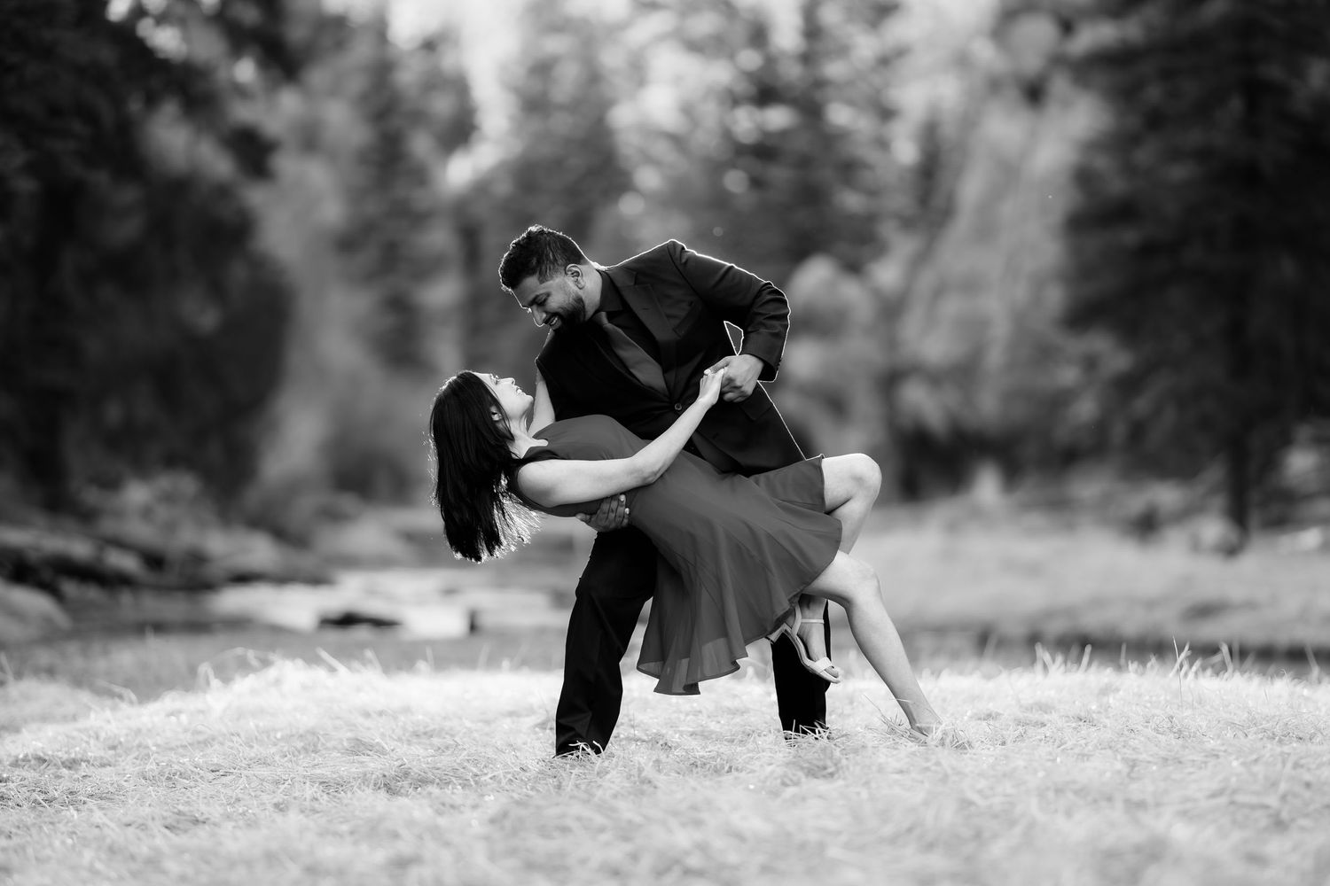 A couple performs a dramatic dance dip pose in a black and white portrait in a forest clearing.