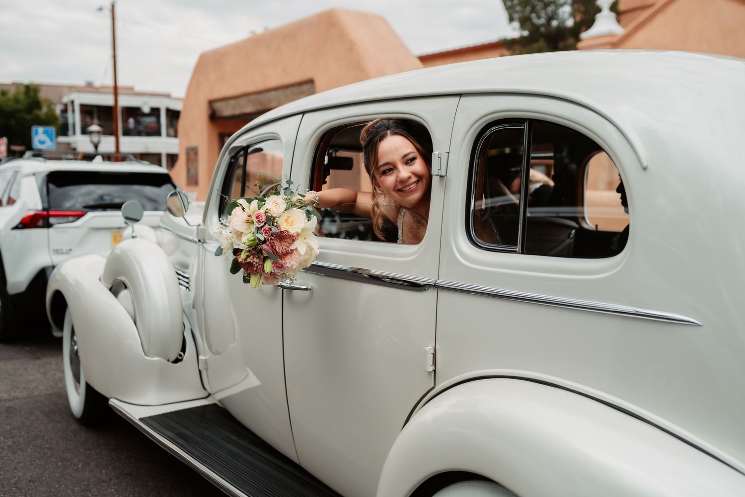 Elegant white vintage wedding car parked outside a building with pink stucco walls.