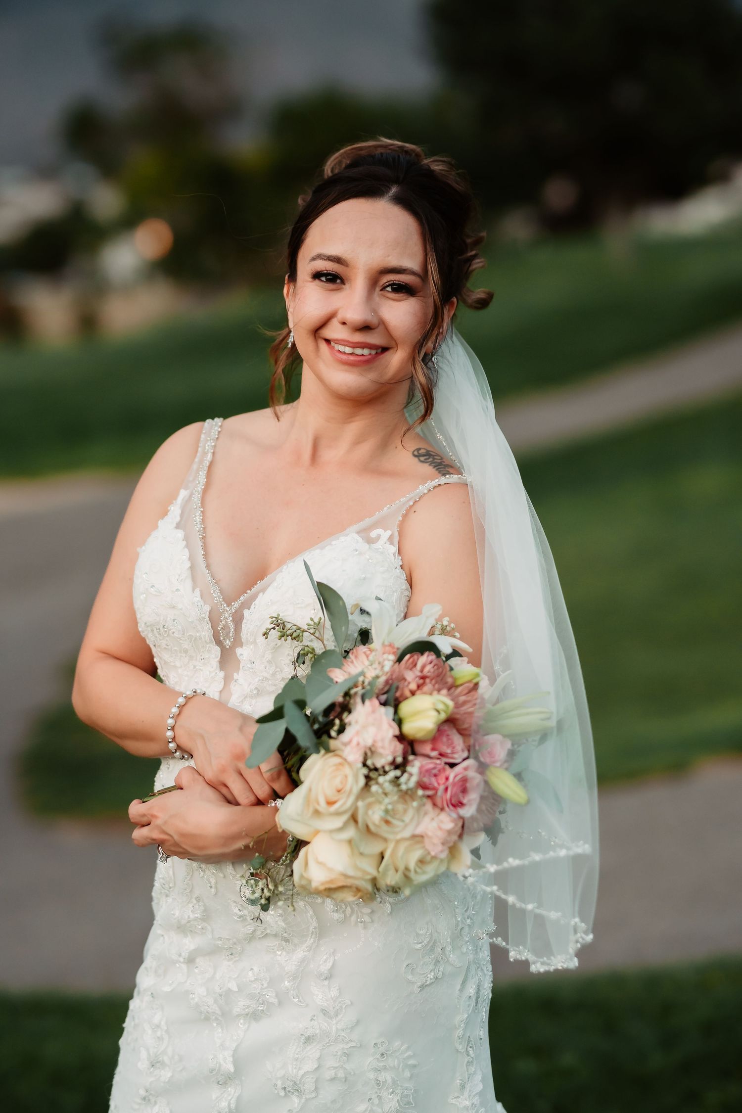 Elegant white lace wedding dress with delicate floral bouquet in outdoor garden setting.