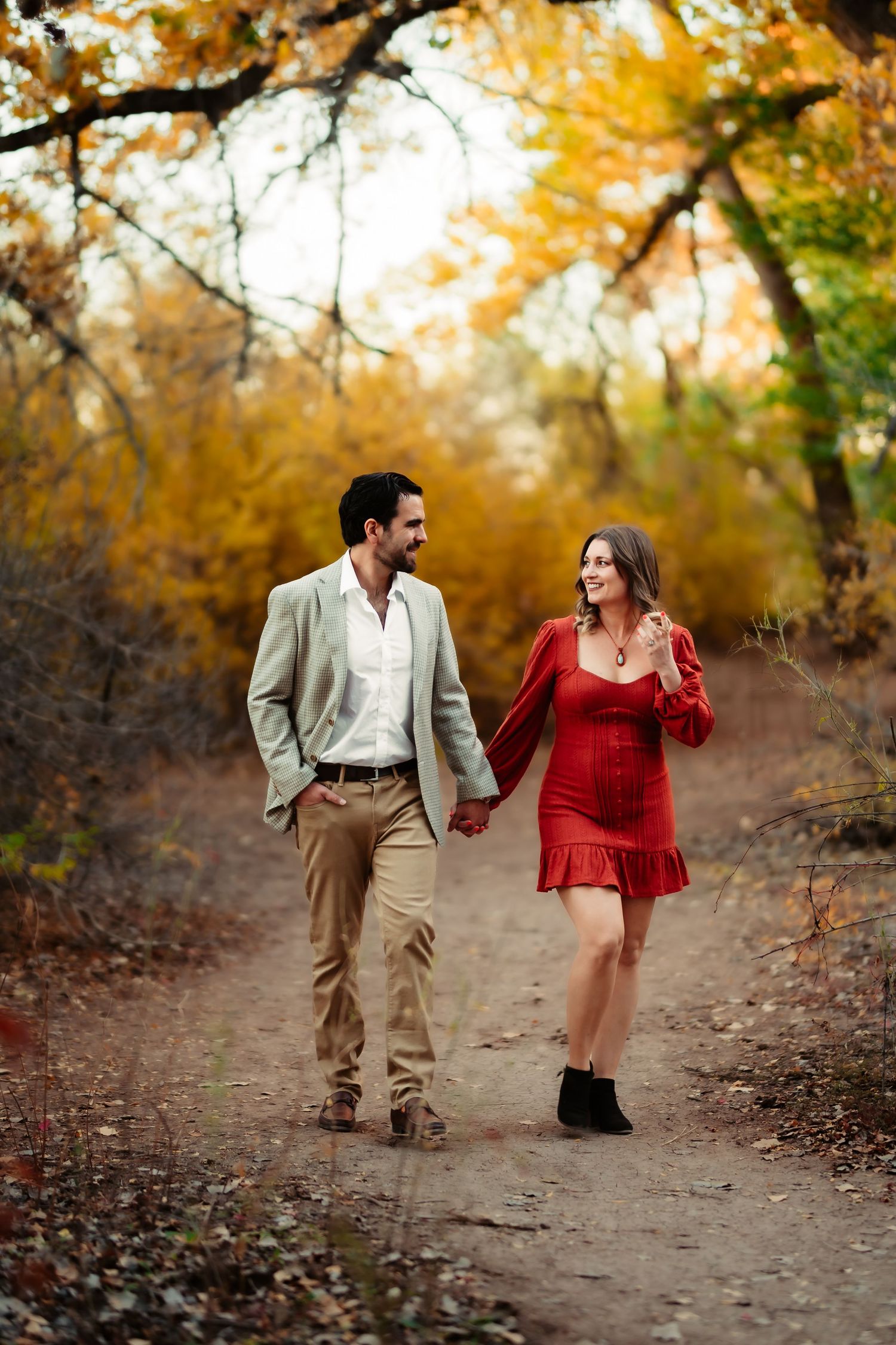 A couple walks together on an autumn trail surrounded by golden trees and fallen leaves.
