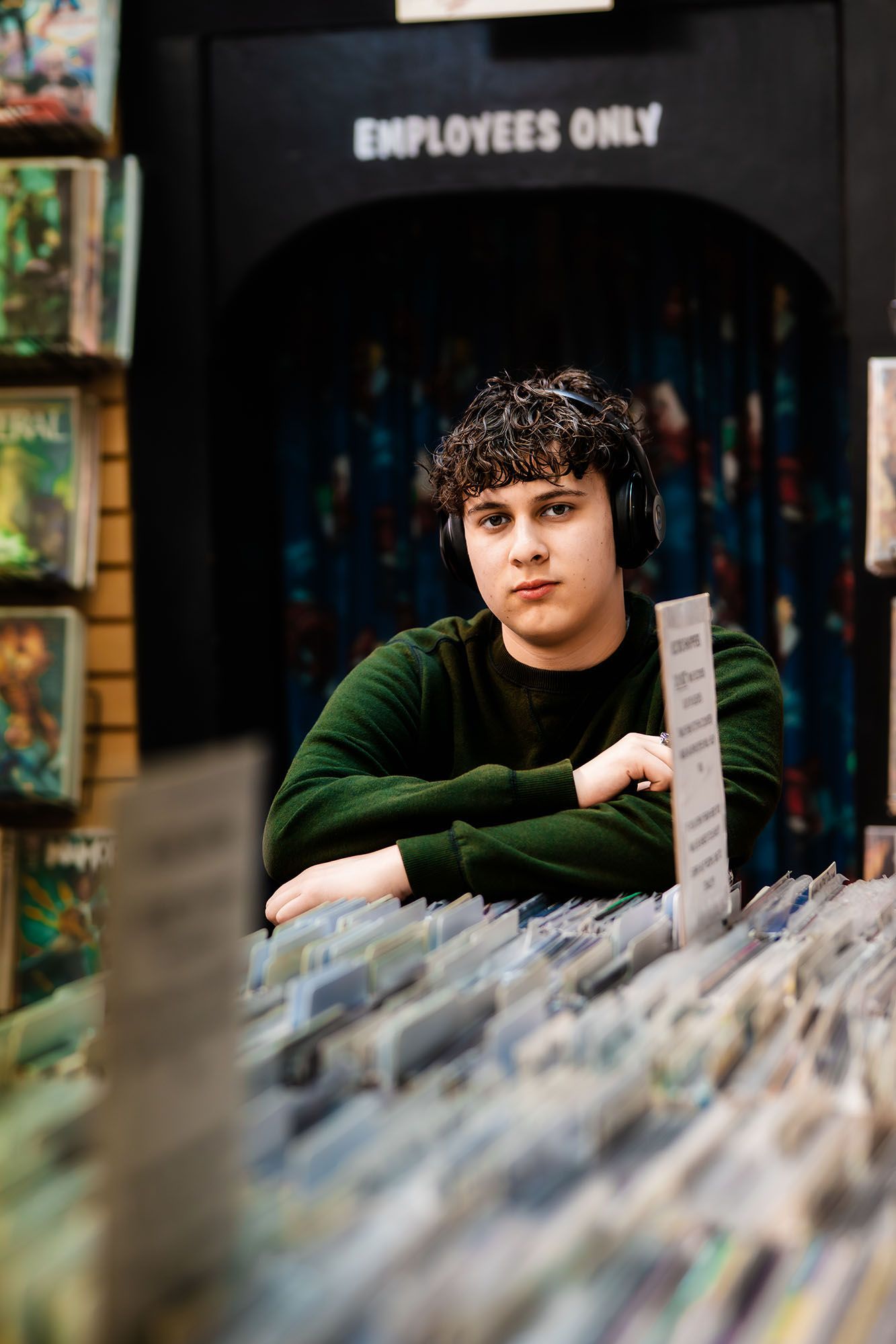 Young man with headphones browses vinyl records in a music store near an Employees Only door.