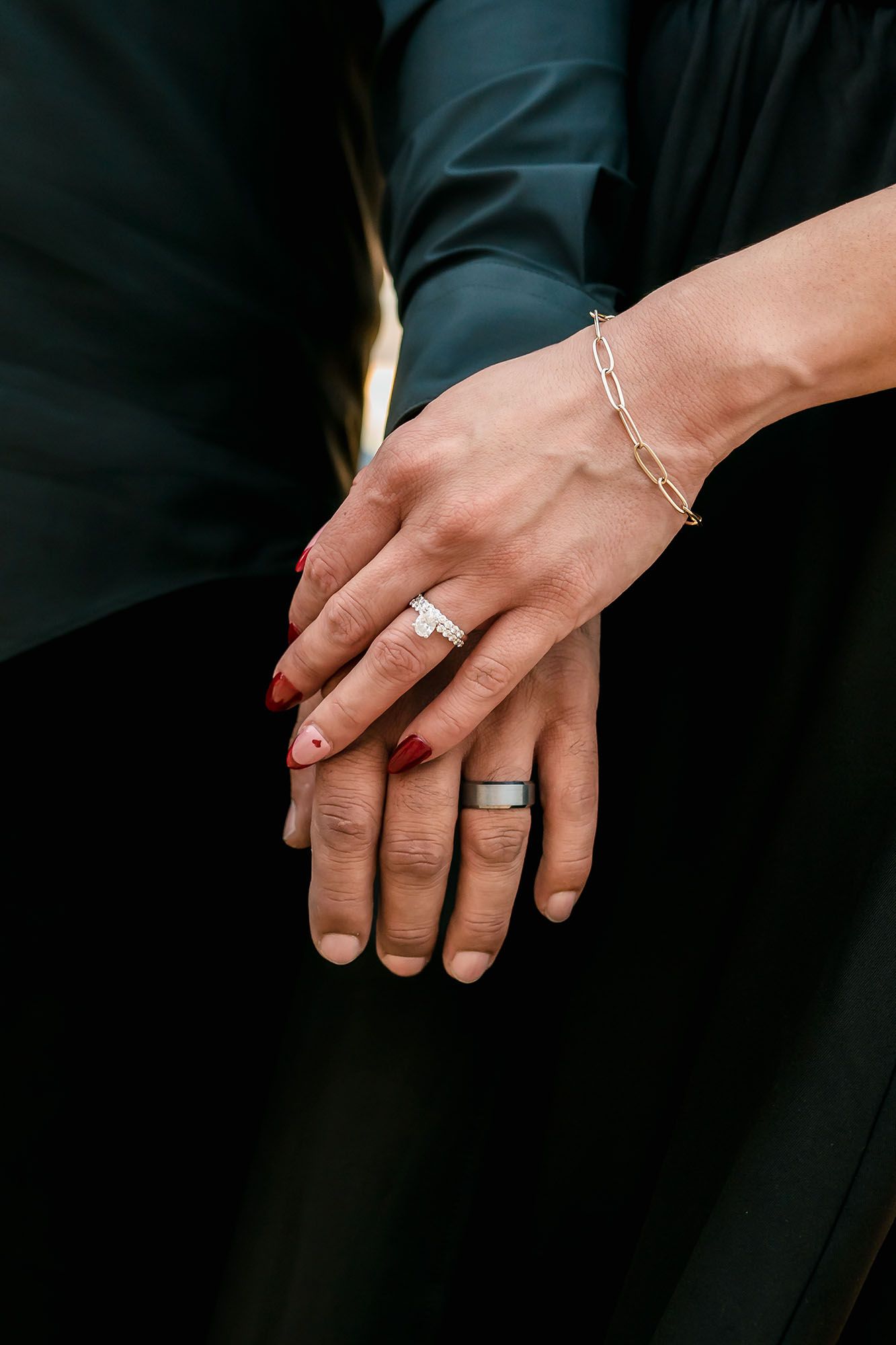 Close-up of couple's hands showing diamond engagement ring, gold bracelet, and wedding band.