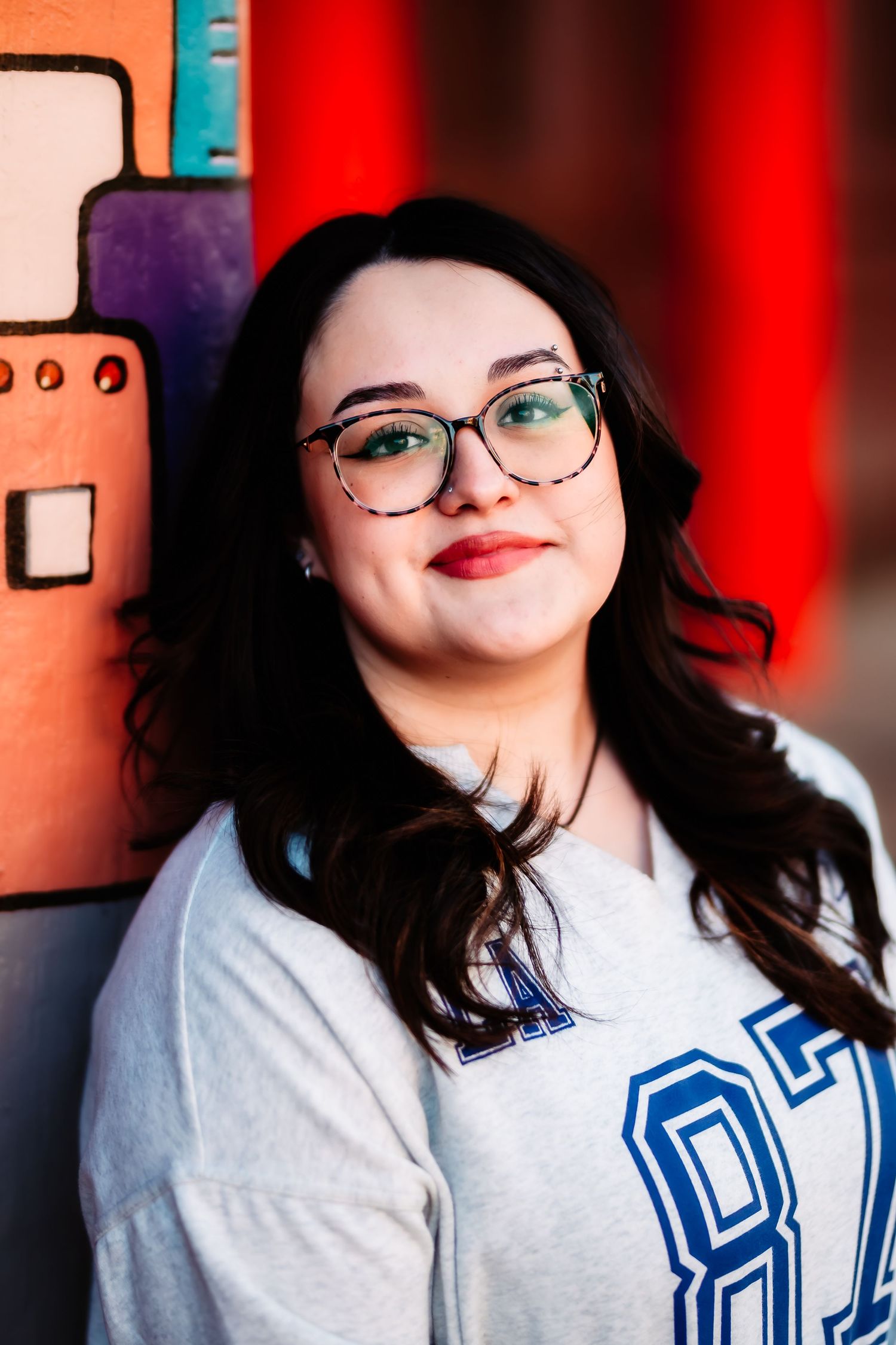 Portrait photo with blue varsity numbers and glasses against red background, soft natural smile.