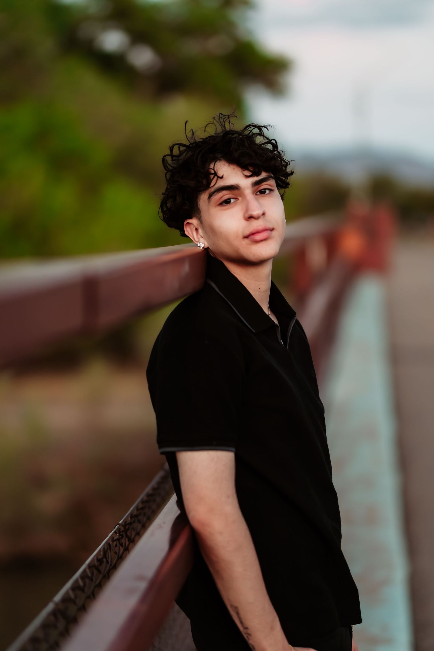 Stylish portrait against a bridge railing at sunset with mountains in the background.