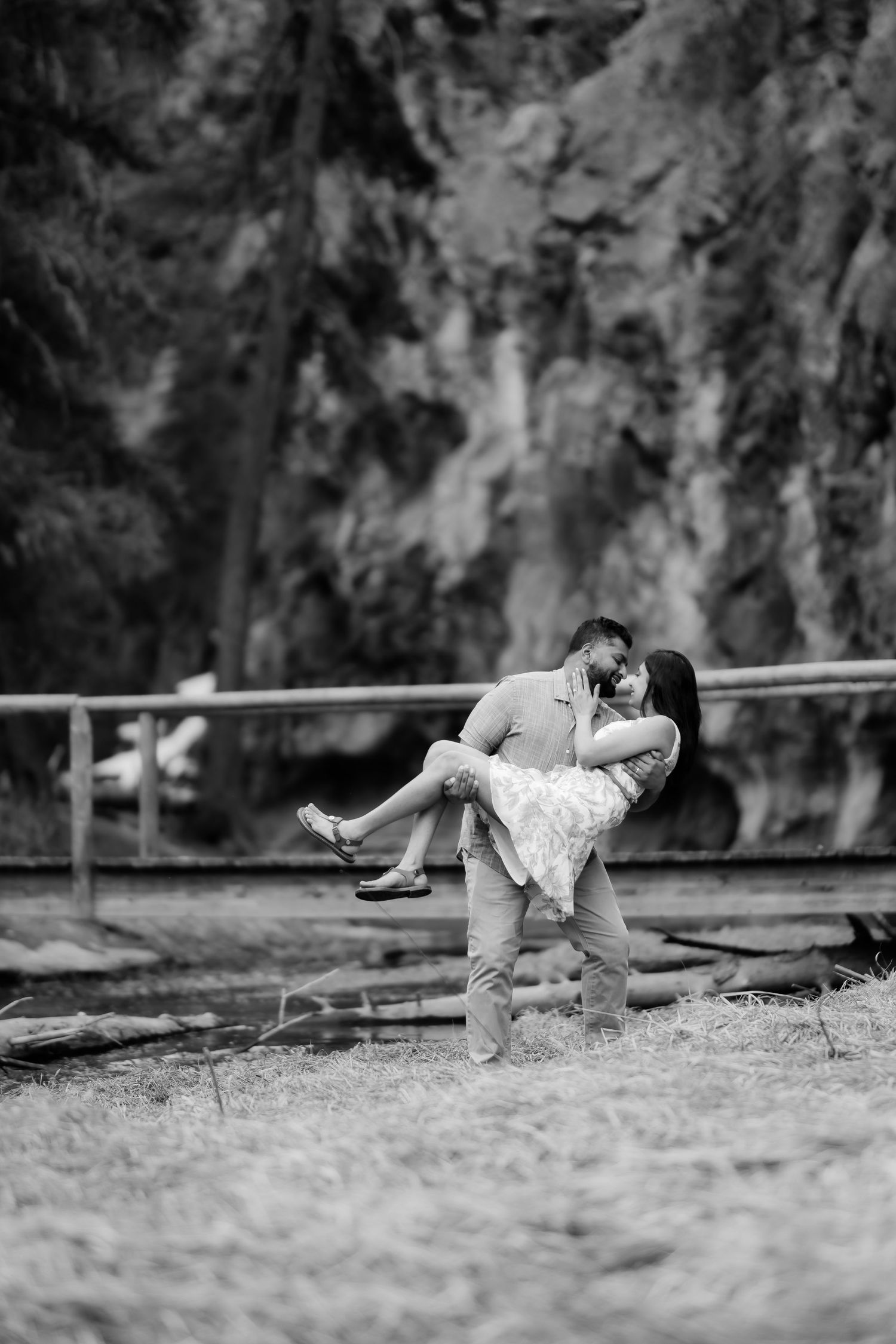 A romantic dip pose captured in black and white photography near a rocky cliff backdrop.