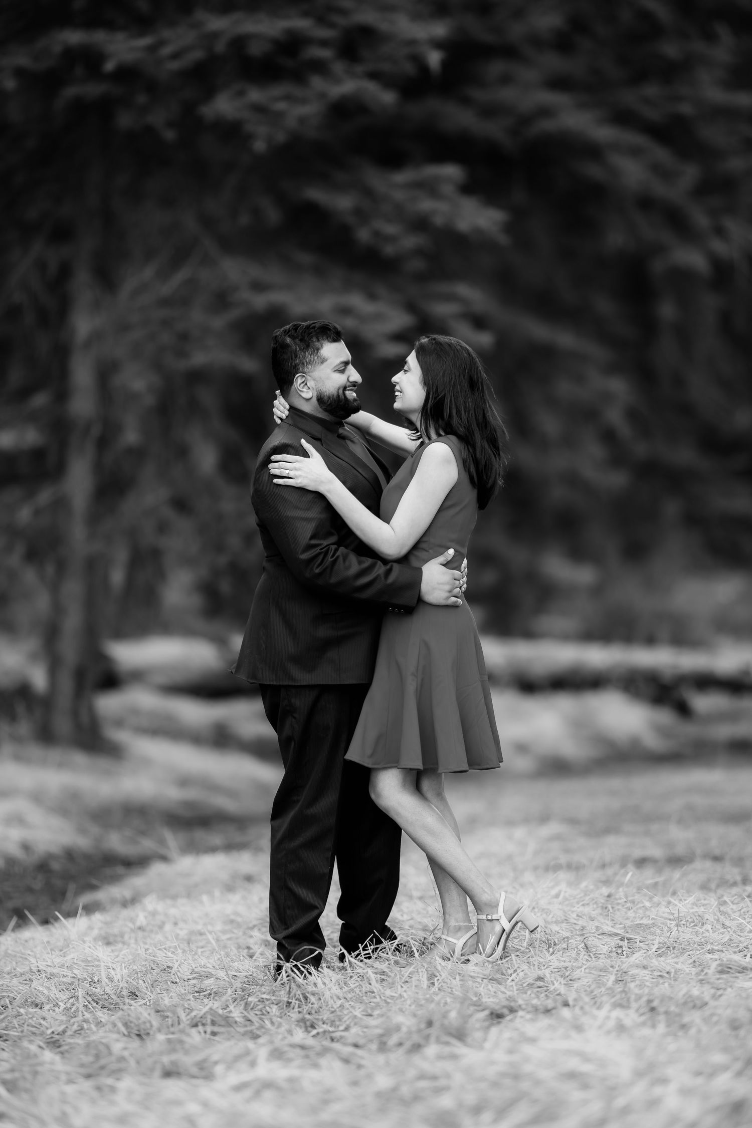 A romantic black and white portrait of a couple embracing in an outdoor setting.