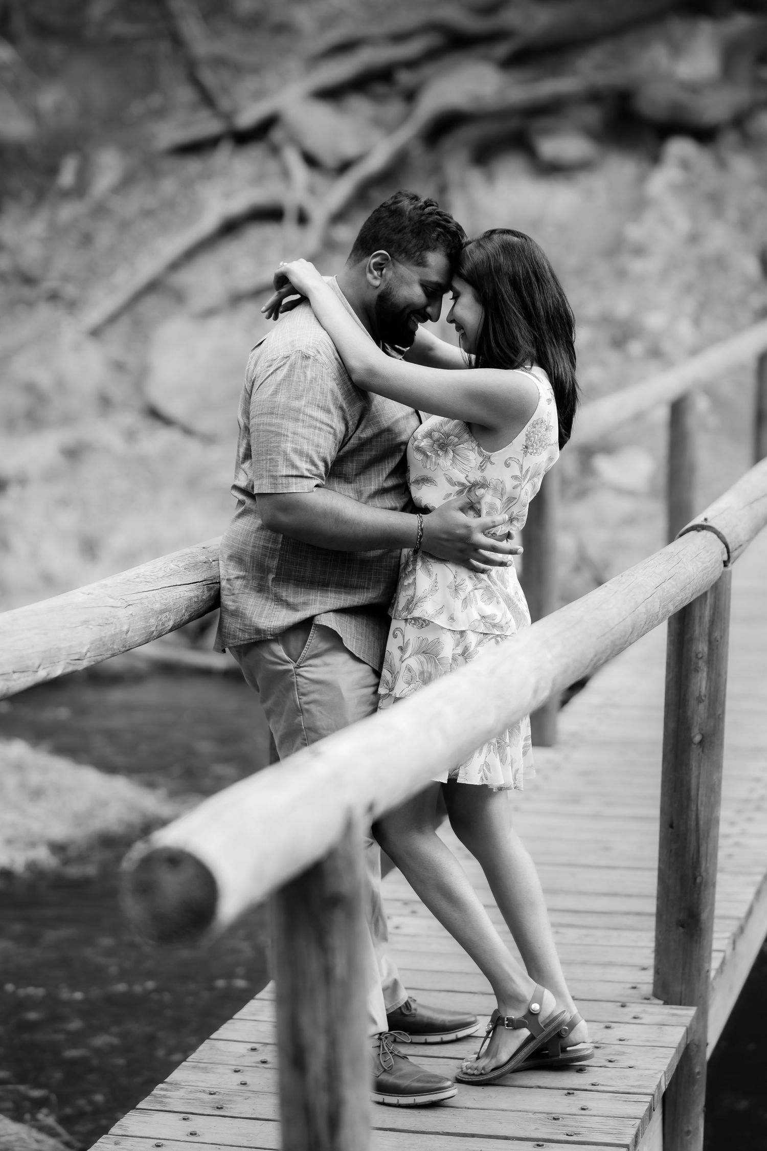 A romantic couple sharing an intimate moment while embracing on a wooden bridge in black and white.