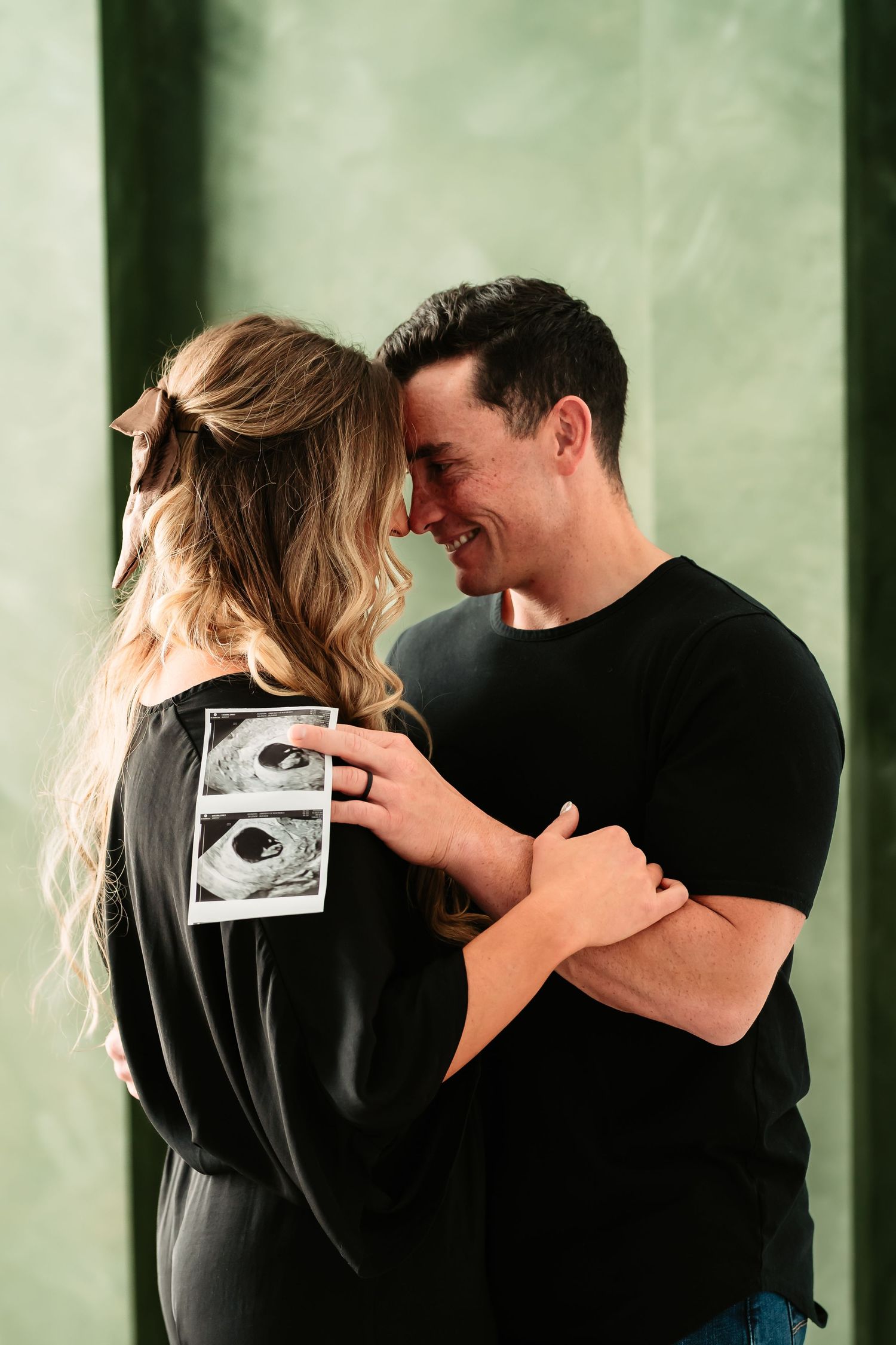 A couple in black clothing shares an intimate moment while holding an ultrasound photo in a sequence of images.