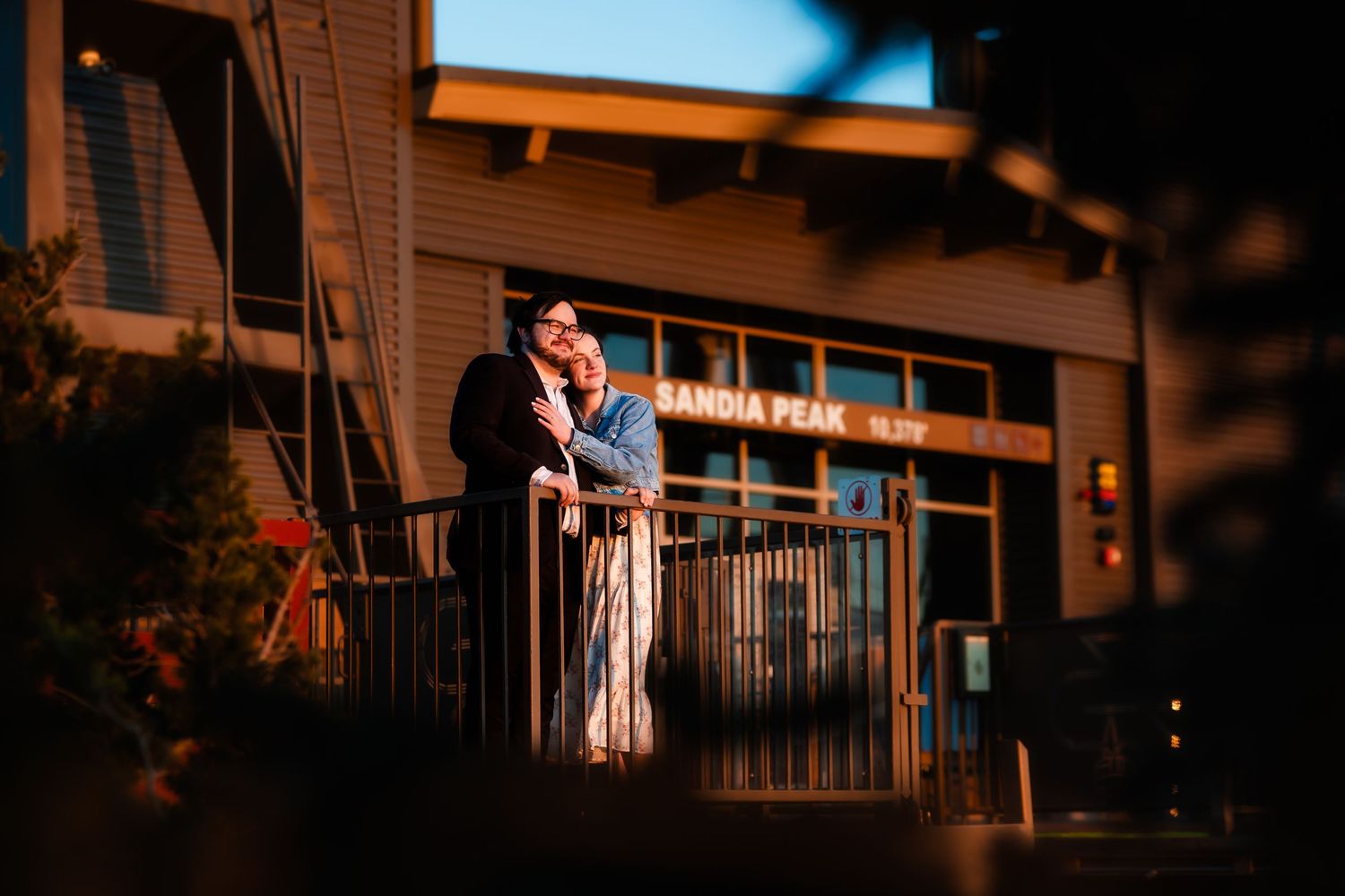 A couple embraces romantically on an apartment balcony during sunset with warm golden lighting.