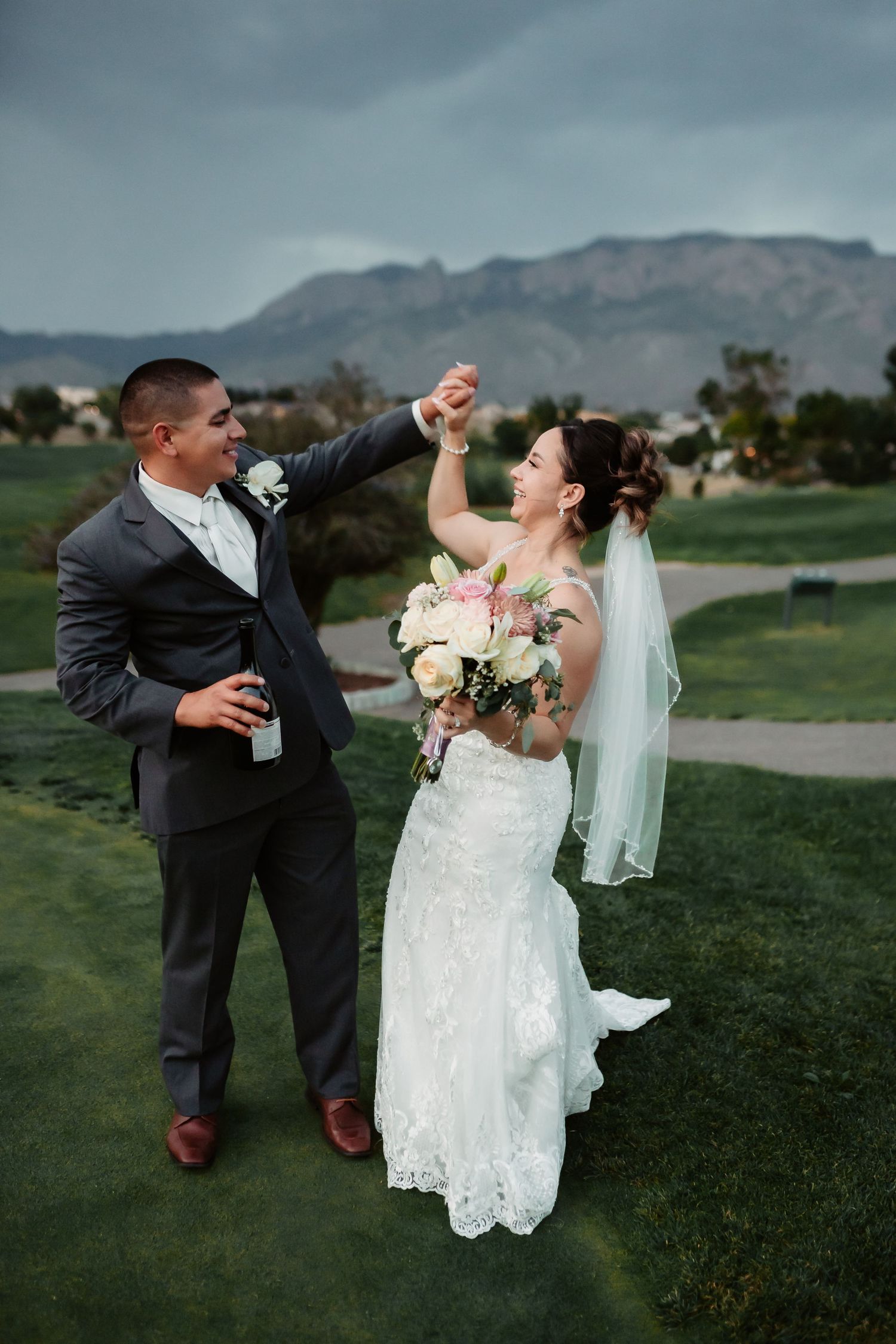 Newlyweds share dynamic dance moves during outdoor wedding photoshoot with mountain views.