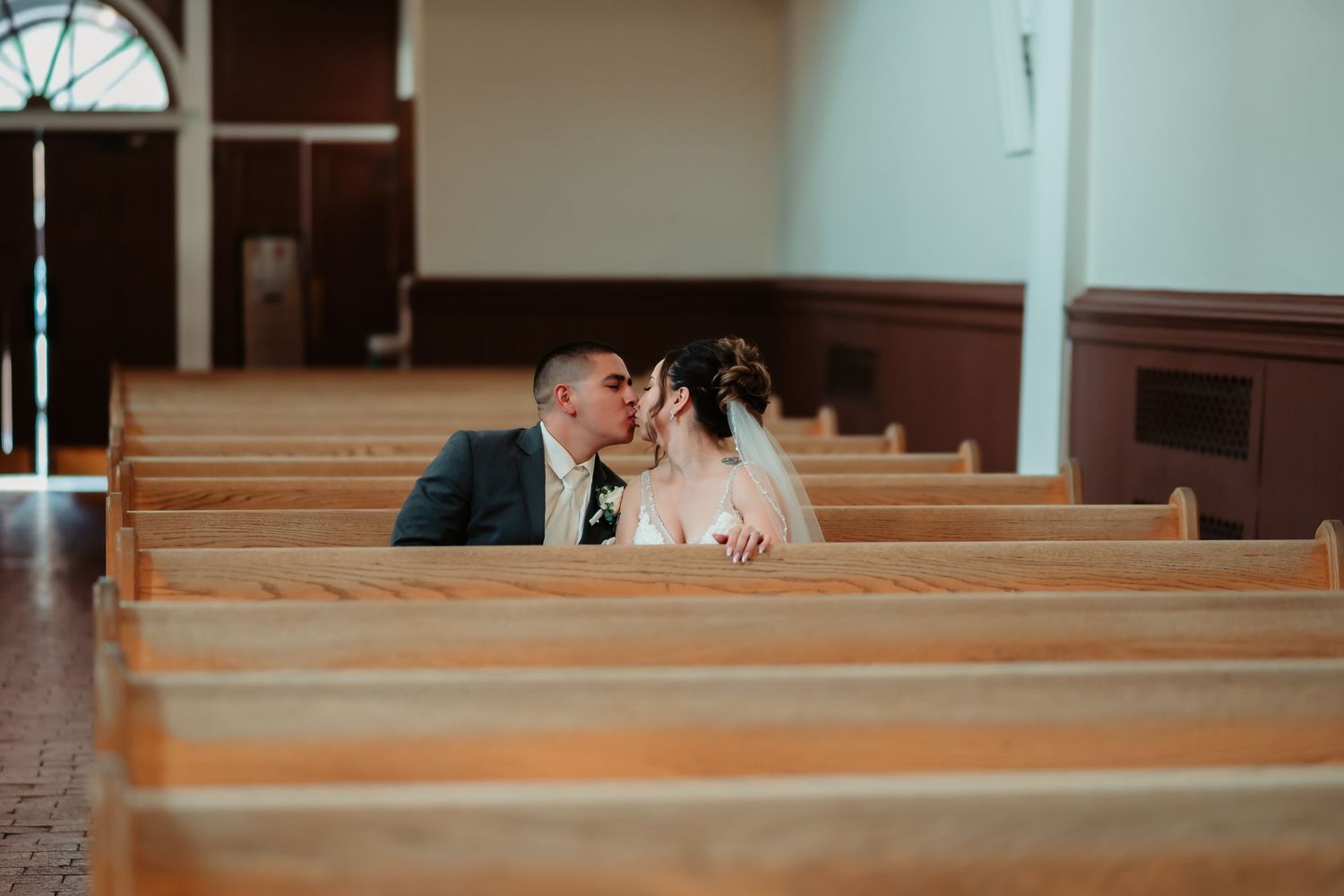Religious interior with wooden church pews and arched windows illuminated by natural light.