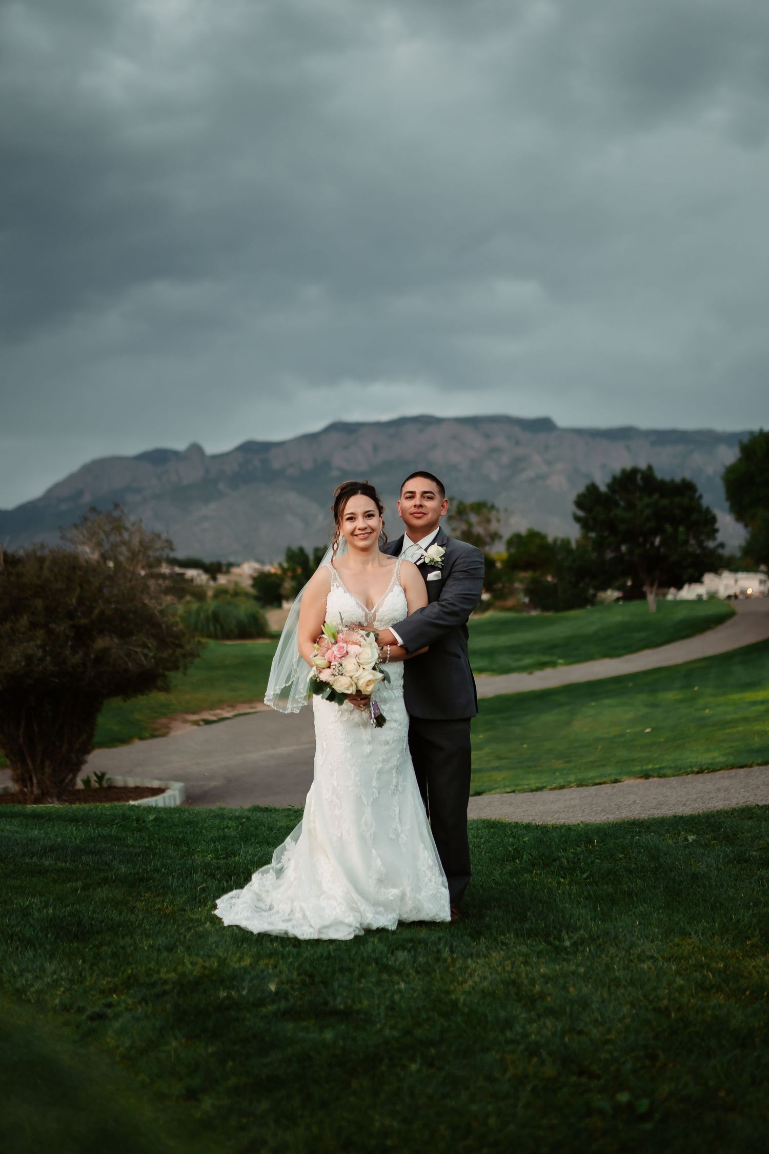 A joyful wedding photo session on a grassy hill with mountain views and cloudy skies in the background.