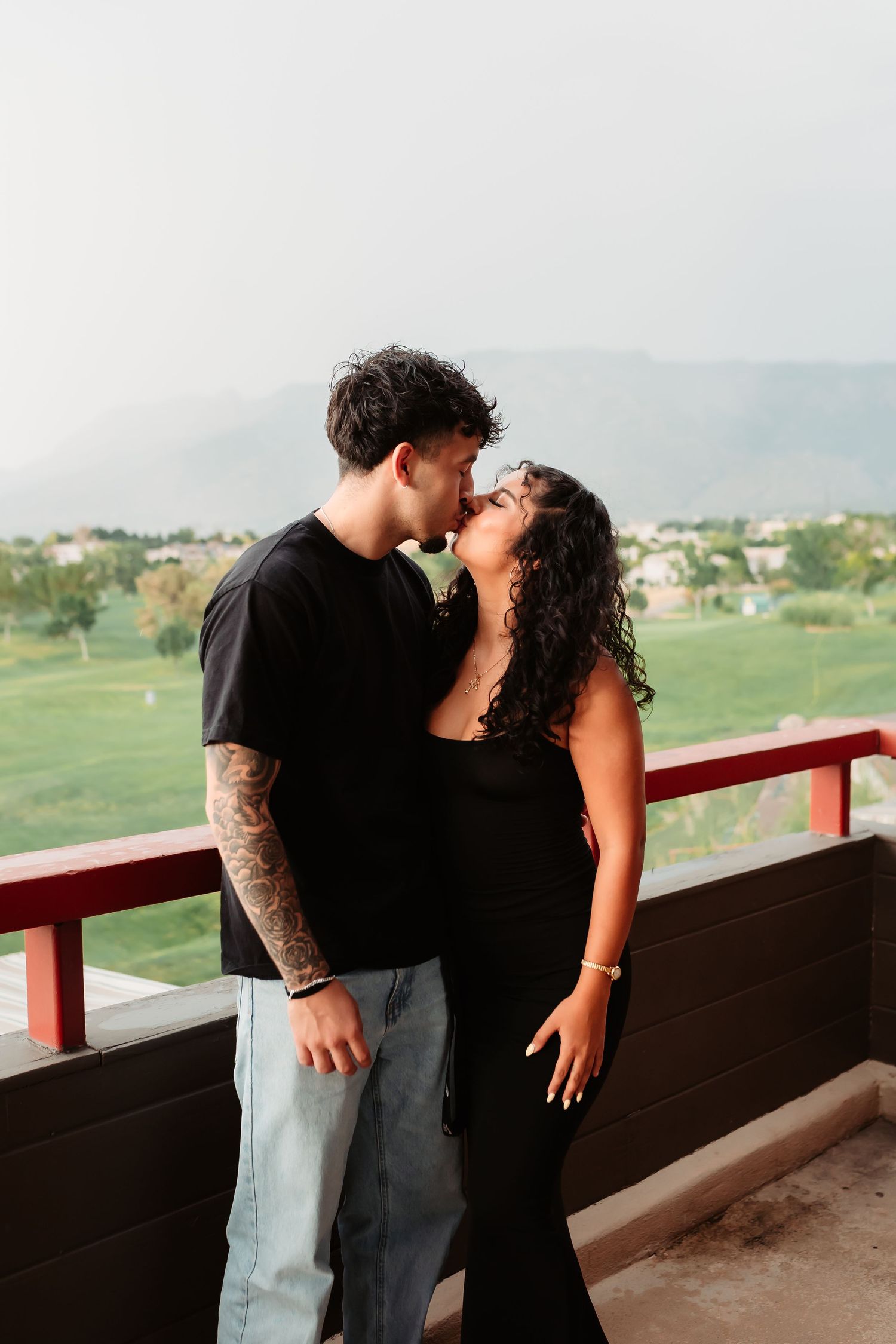 Couple sharing an intimate moment on an outdoor balcony overlooking a scenic landscape.