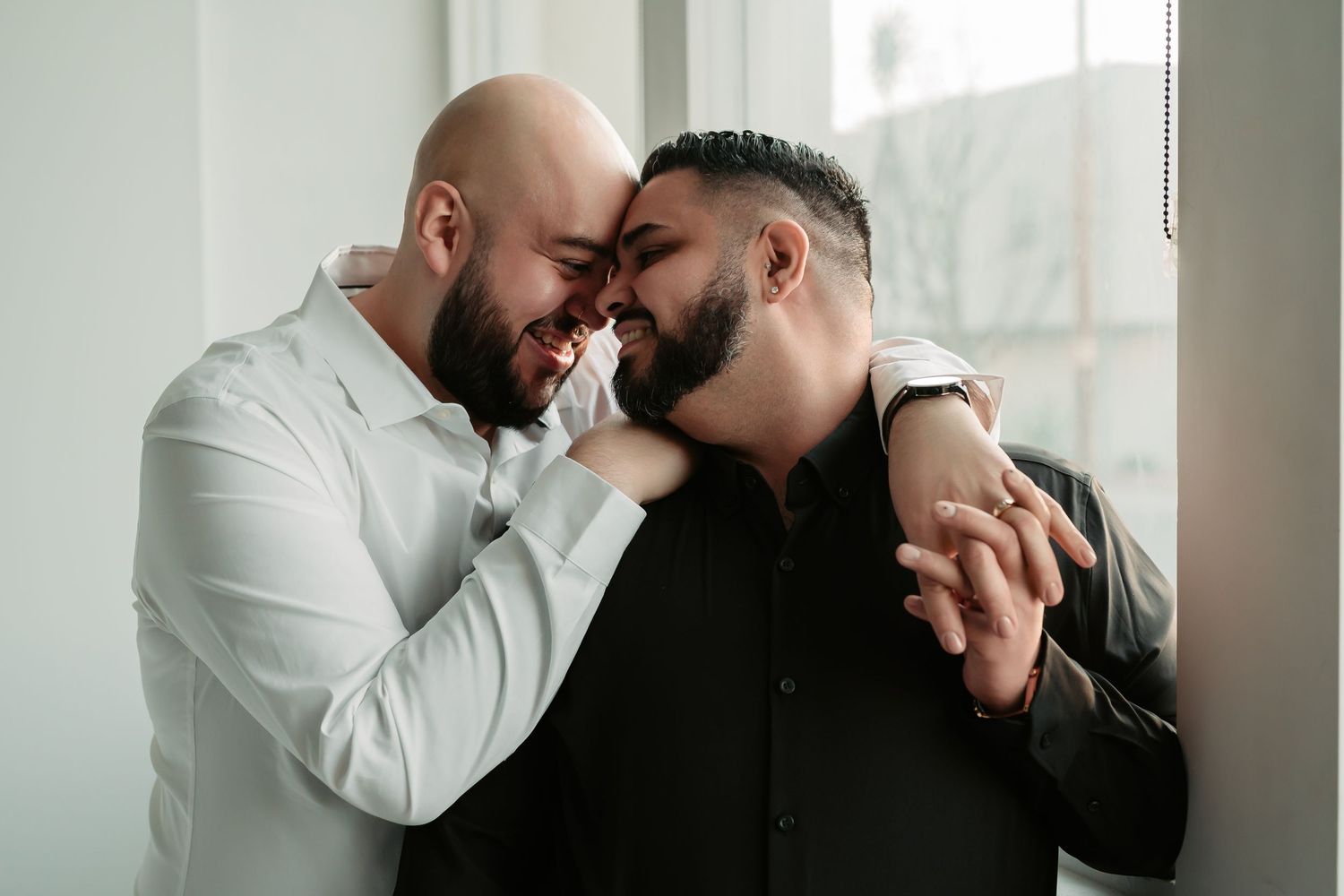 Two people share an intimate moment together near a window with soft natural lighting.