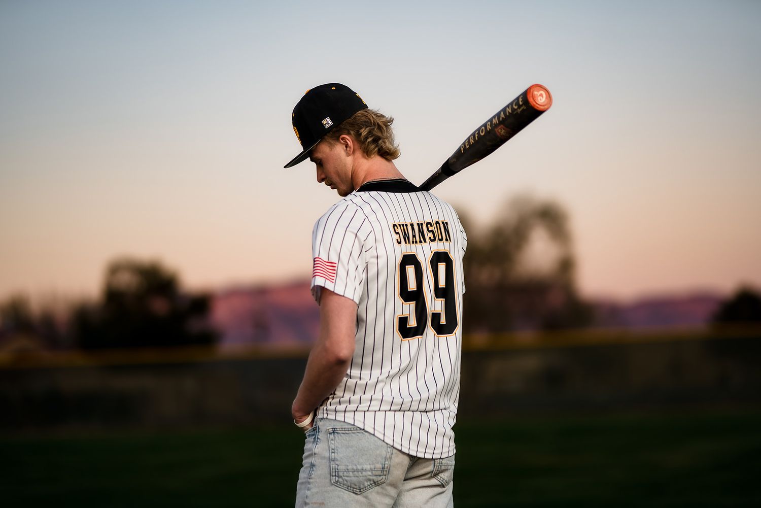 Baseball player in pinstripe uniform stands ready at bat during sunset practice session.