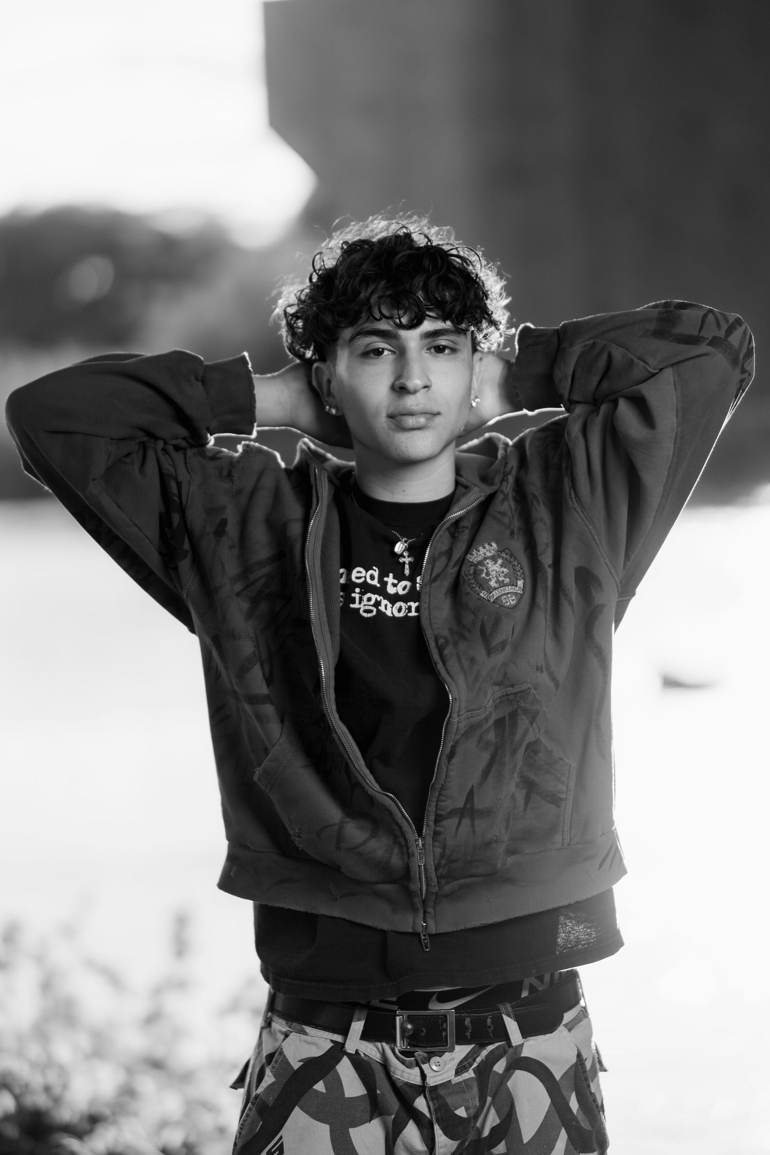 Black and white portrait of someone wearing a sweatshirt and camo pants in natural backlit lighting.