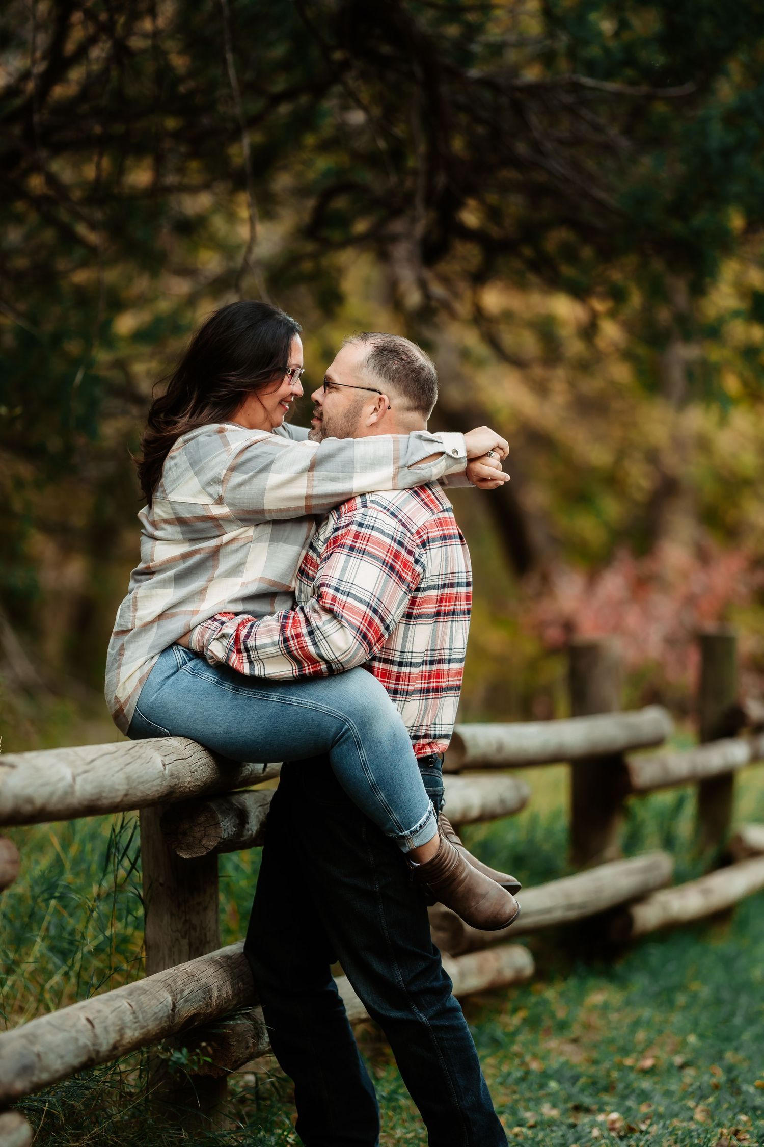 Romantic couple embraces while sitting on rustic wooden fence in autumn forest setting.