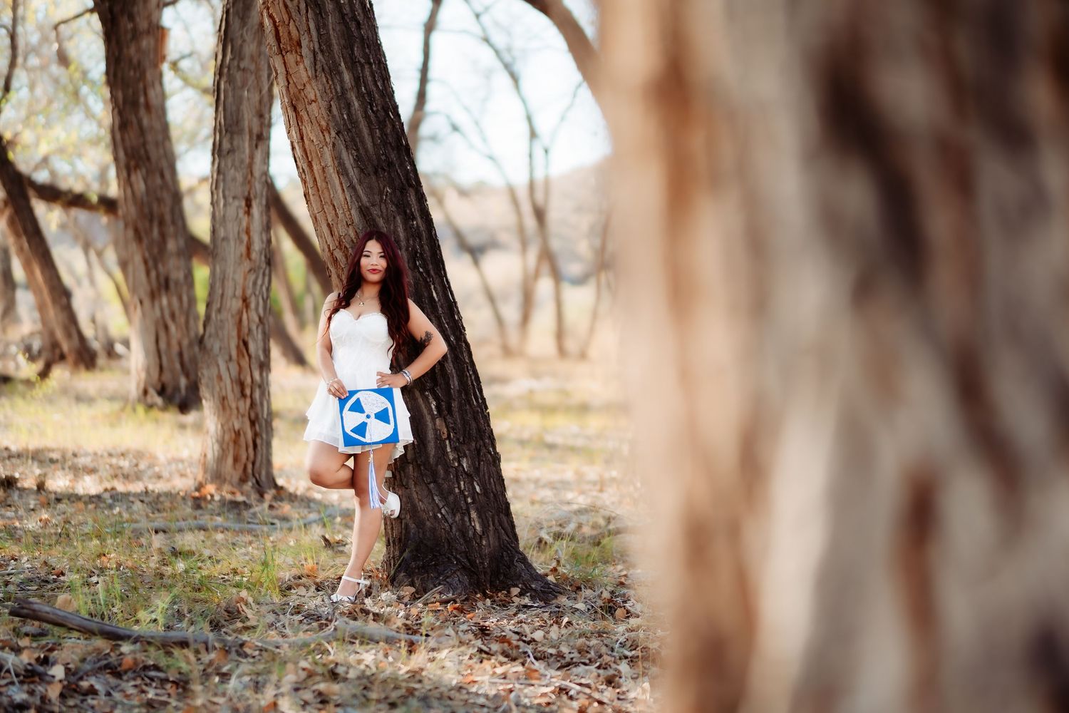 Nature photoshoot featuring person in white dress posing by tree trunk in autumn setting.