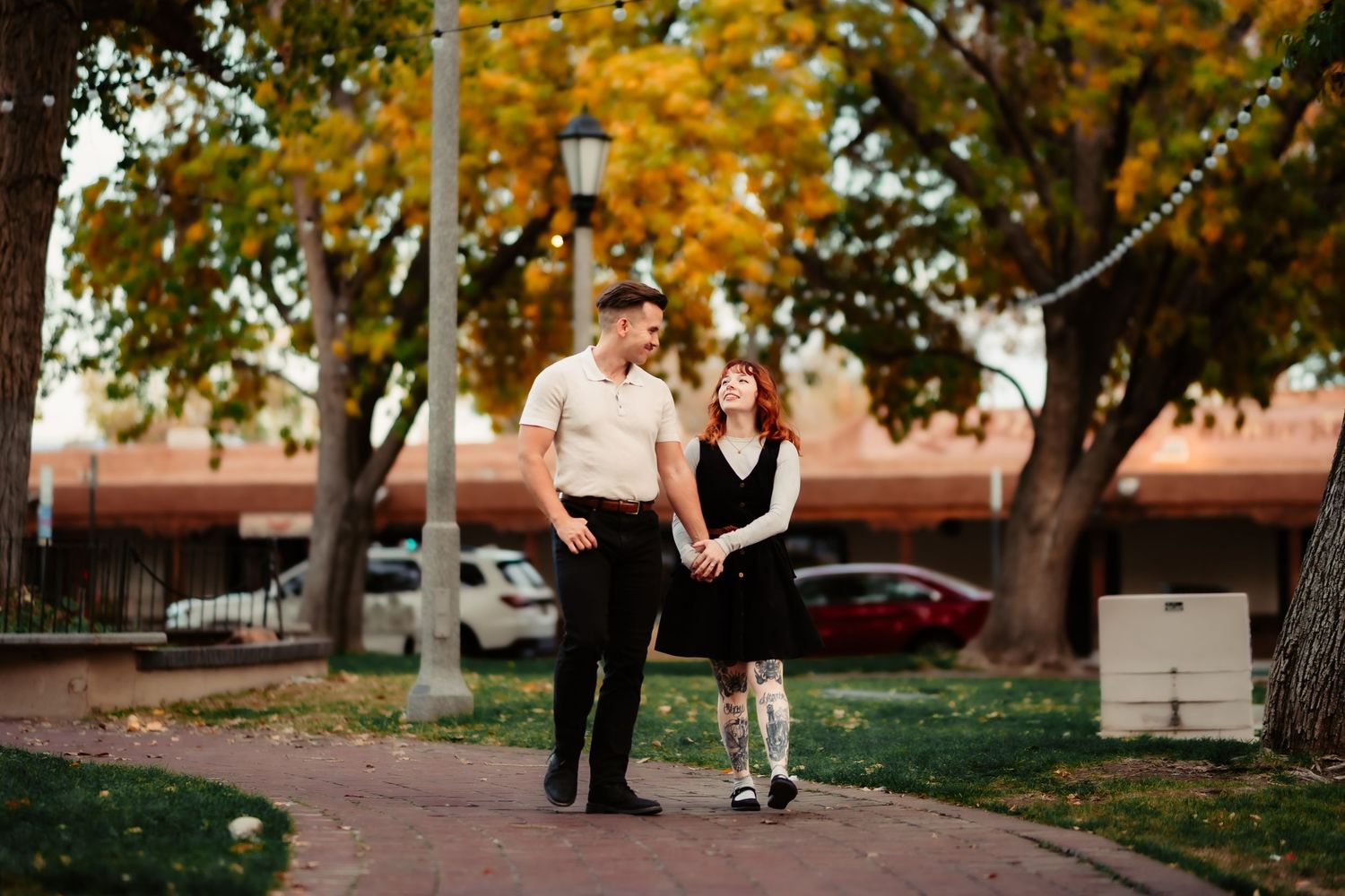 A couple walks their dog through a tree-lined path during a golden autumn afternoon.