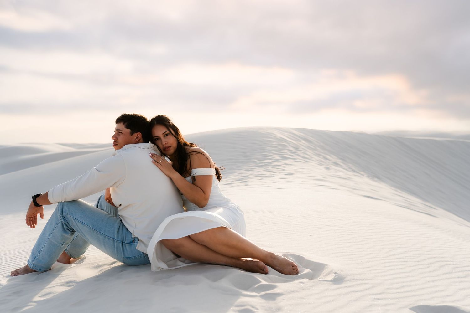 A person in white clothing lies gracefully on pristine white sand dunes during sunset.