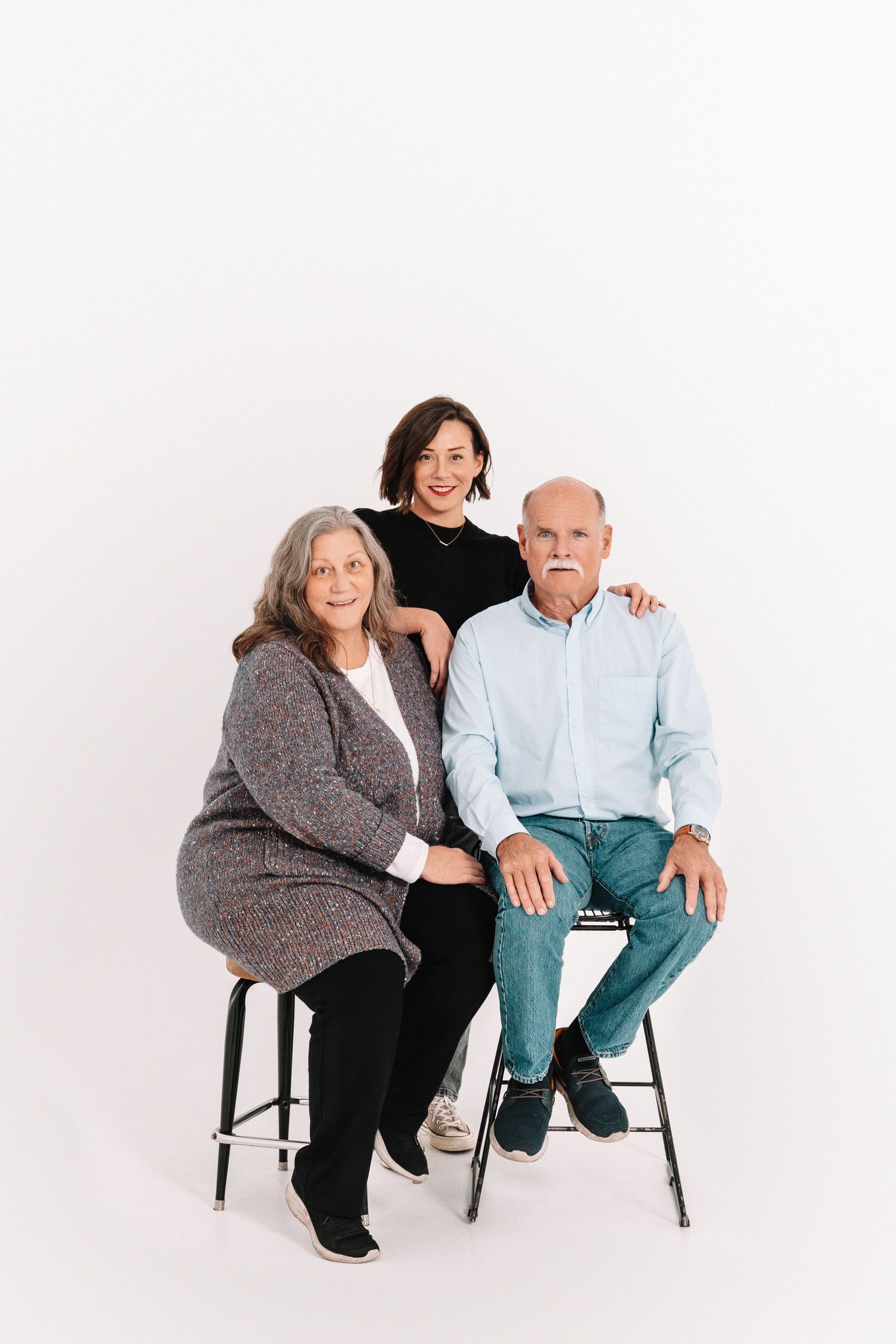 Three candid poses of a couple sitting together on black chairs against a white background.