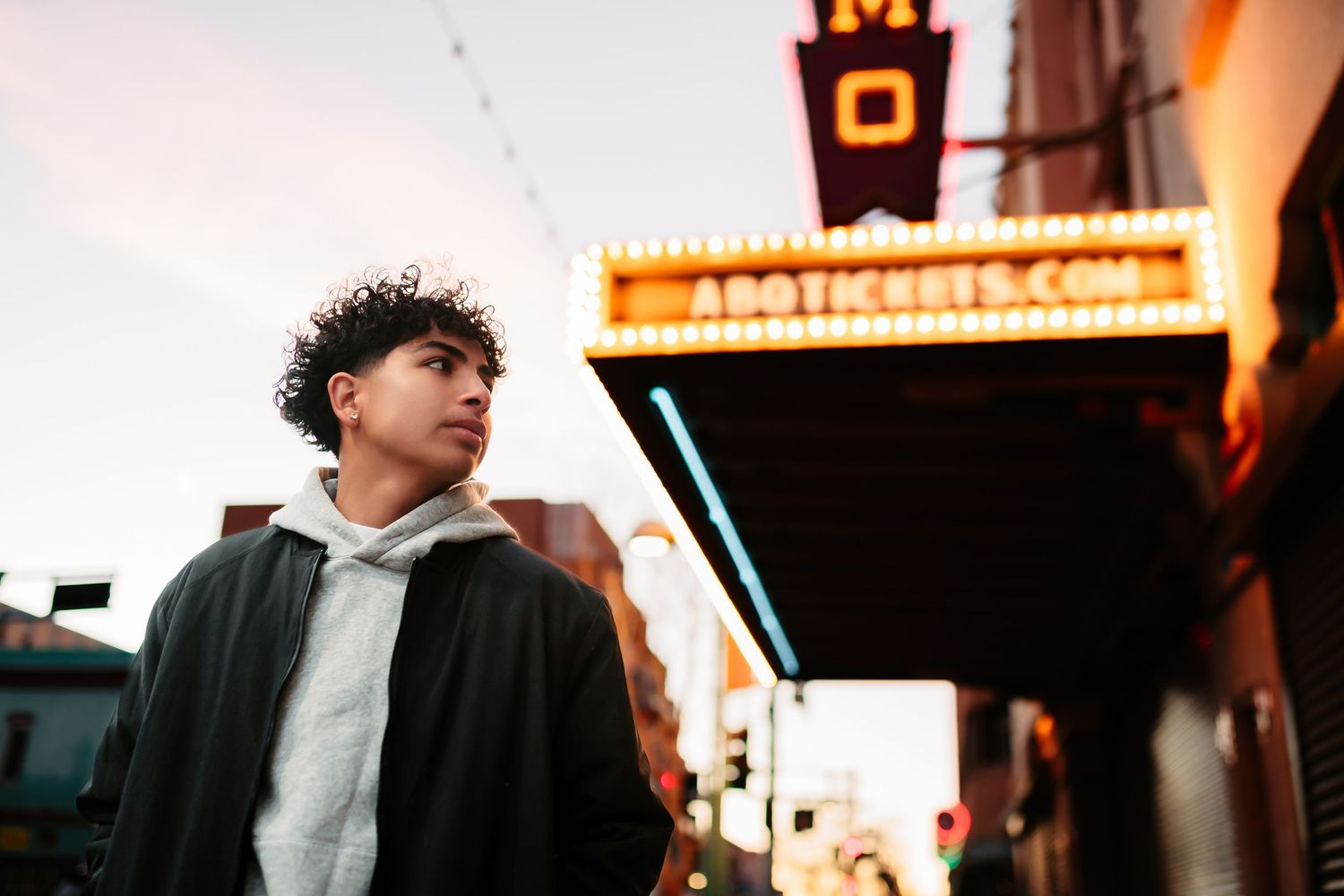 Urban nighttime portrait with illuminated storefront signs and warm lighting creating moody atmosphere.