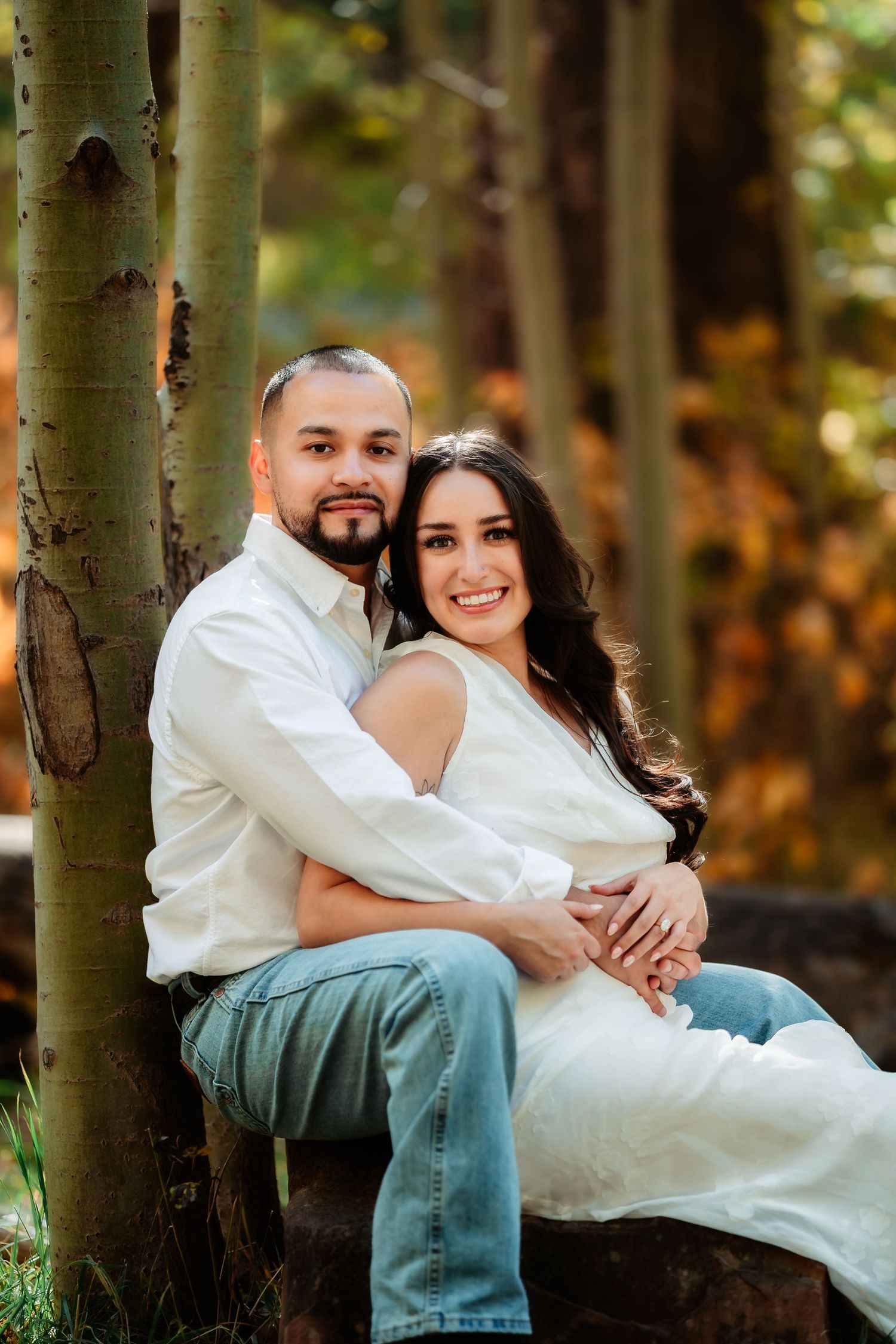A couple in white and blue casual attire poses together among aspen trees during an autumn engagement photoshoot.