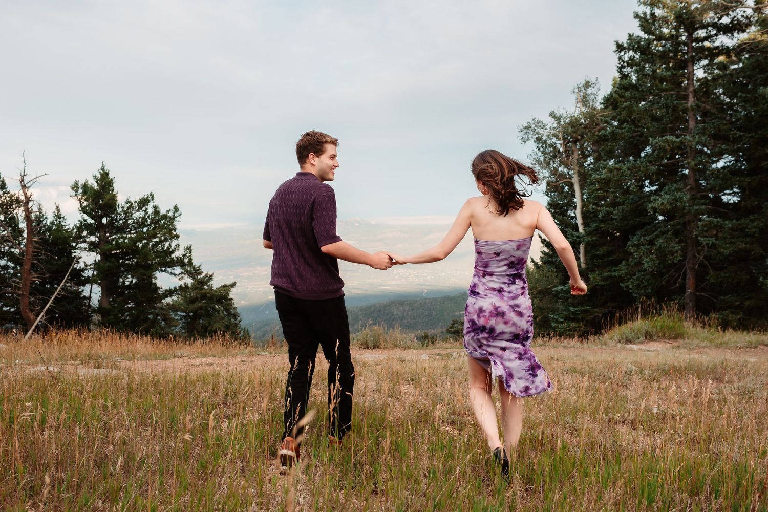 Couple dances and spins together in rustic mountain field during outdoor photo session.