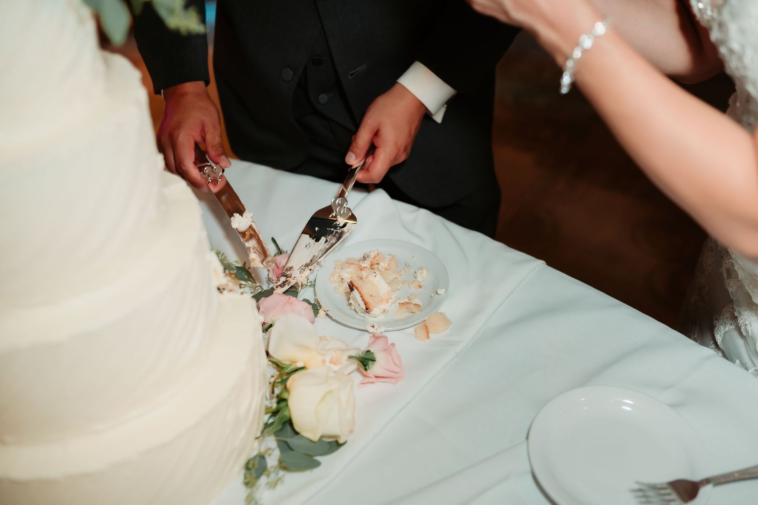 Close up view of white wedding cake being cut into slices.