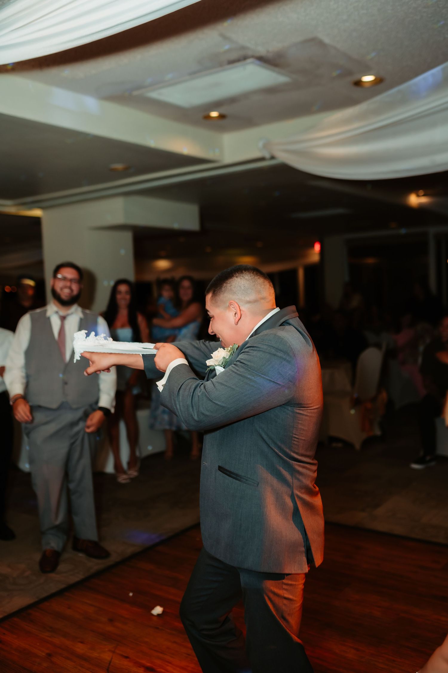Energetic dancing during wedding reception on hardwood floor with guests watching in background.