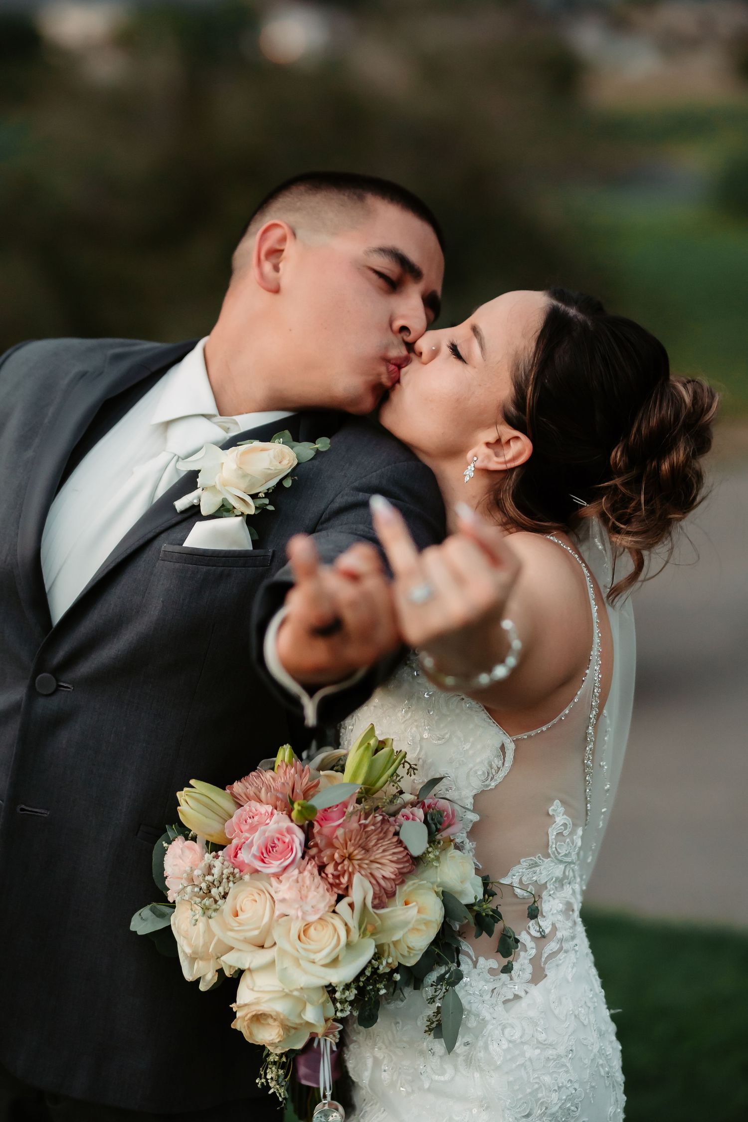 Romantic wedding couple sharing an intimate kiss while holding a beautiful floral bouquet.