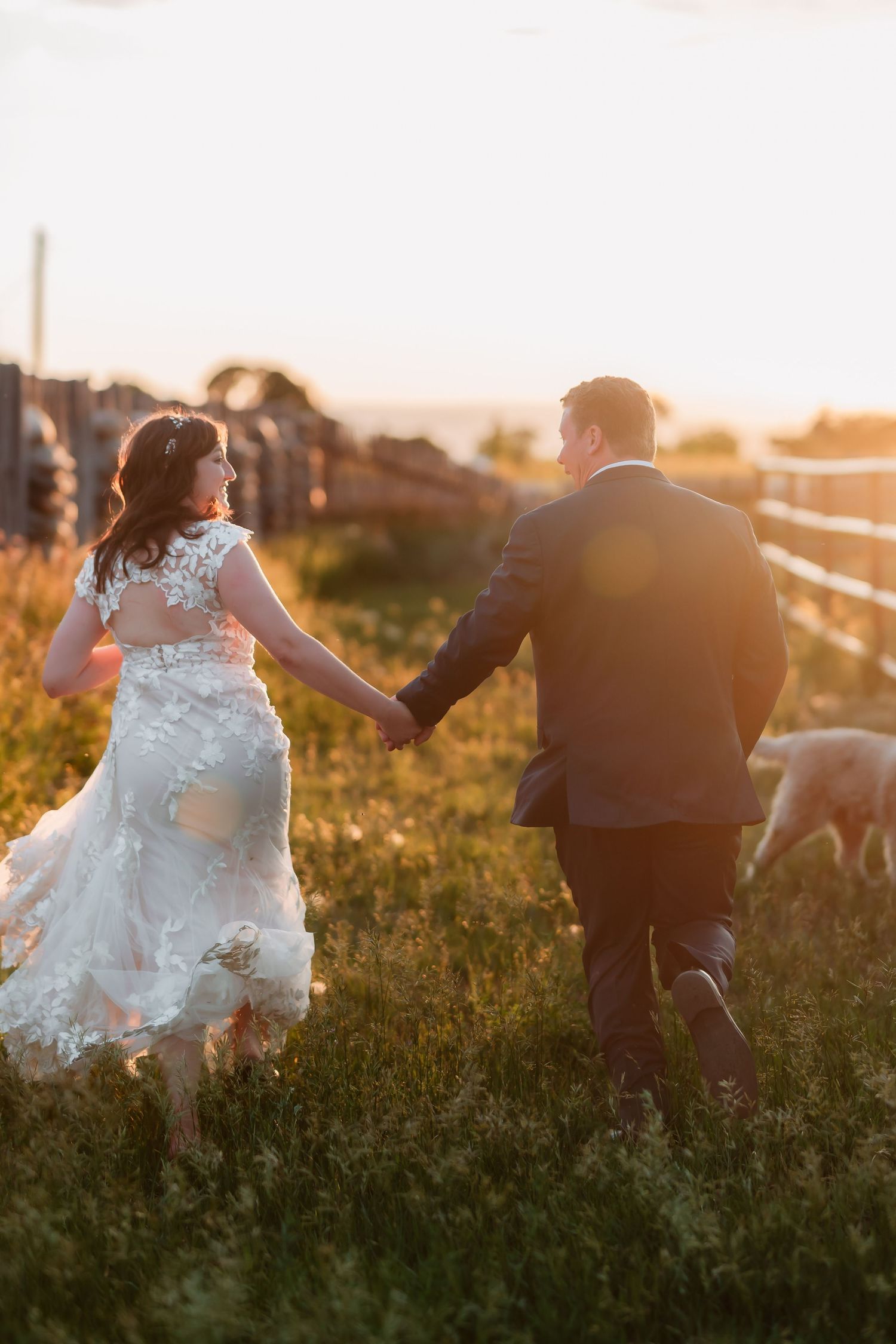 Wedding couple sitting in a golden sunset field with flowing white dress and romantic lighting.